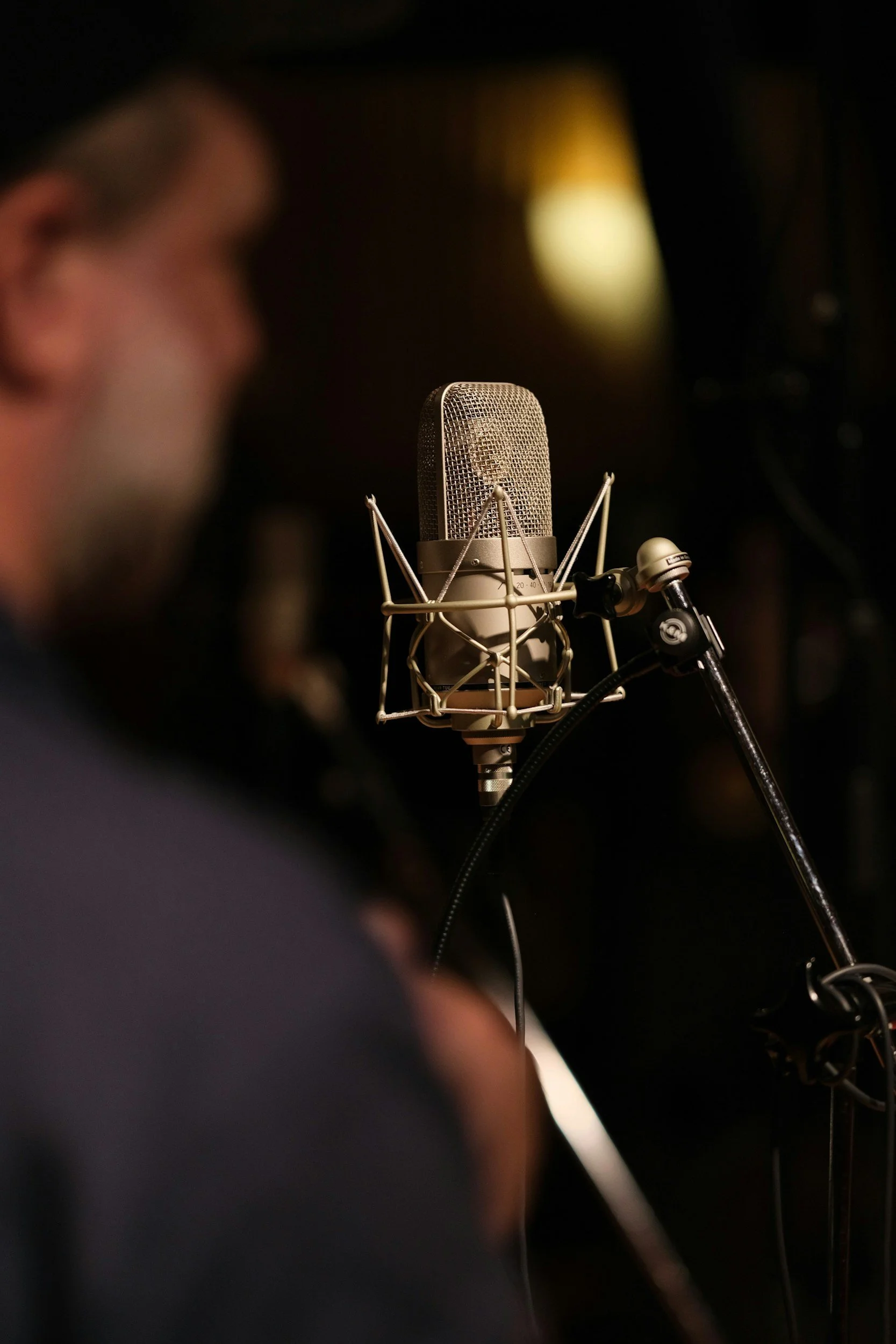 Close-up of a professional microphone in recording studio, with blurred person in background.