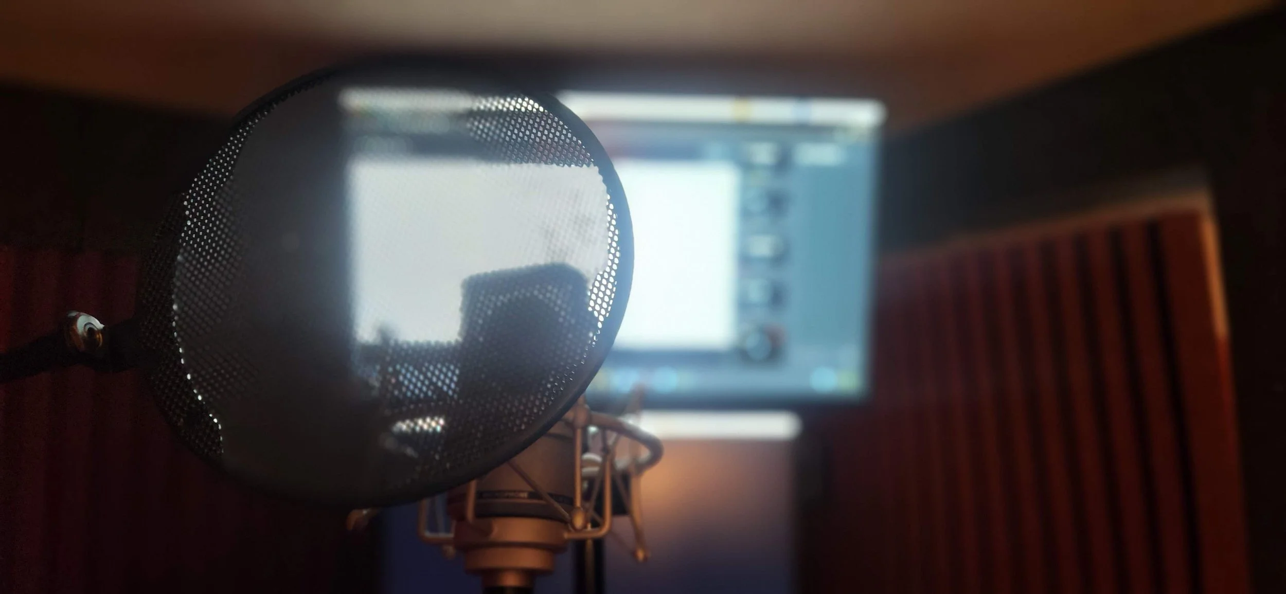 A close-up view of a microphone with a pop filter in front of a computer screen displaying a webpage, on a wooden desk.