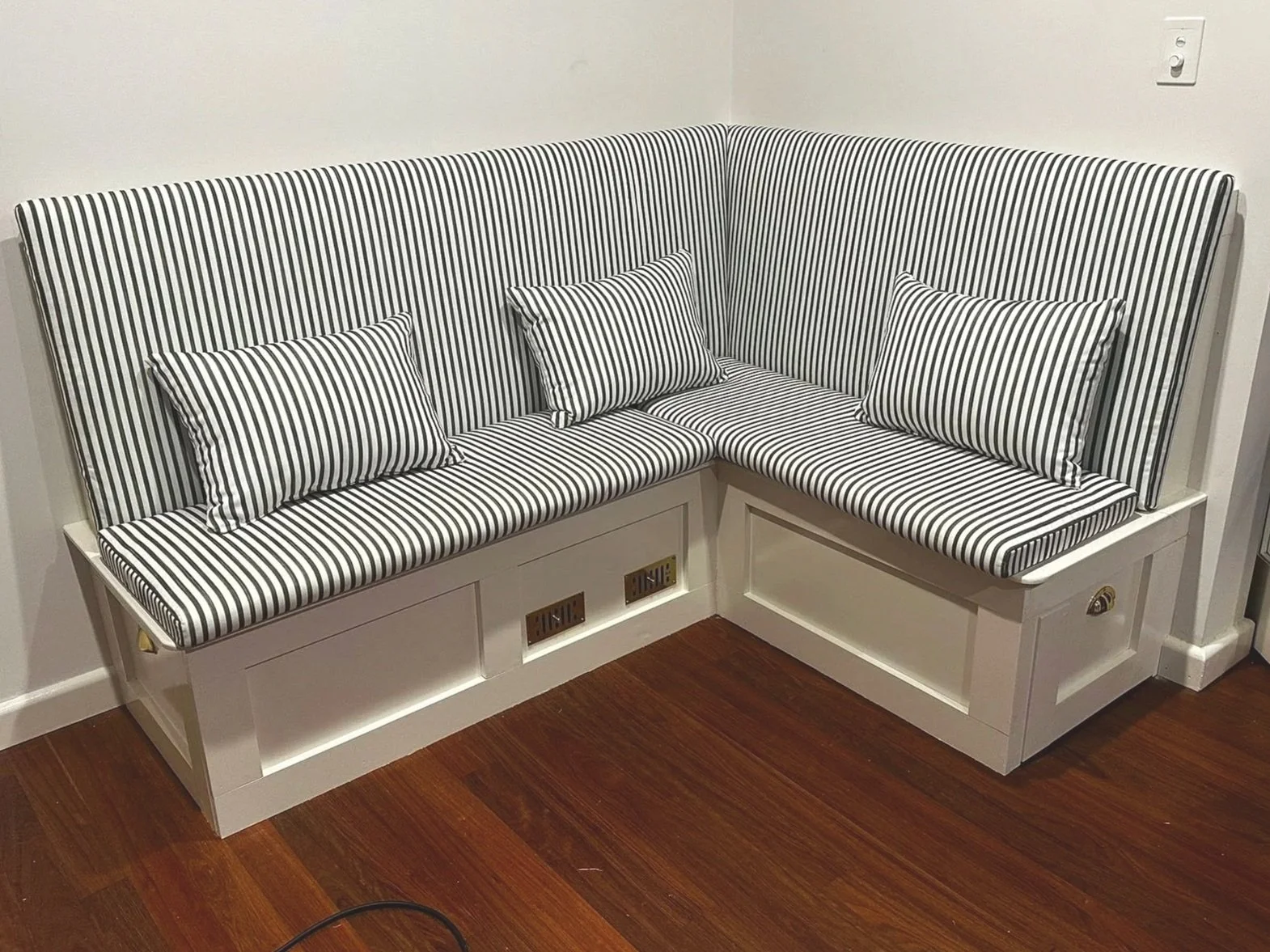 A built-in corner bench with striped black and white upholstery and three matching striped pillows, situated against white walls and a wooden floor.