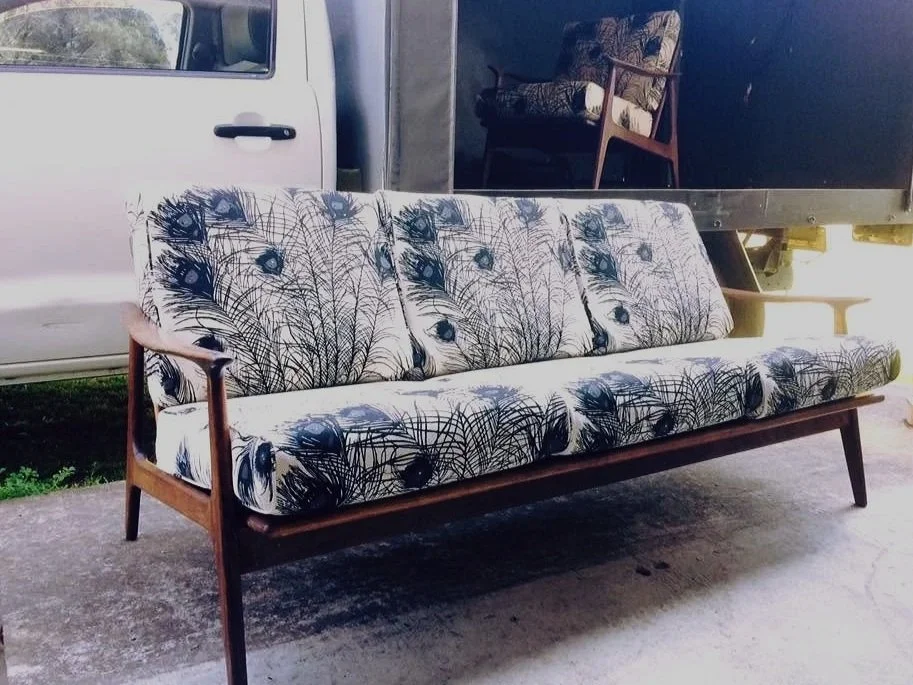 A mid-century modern sofa with a black and white feather pattern on the upholstery, set outside on a concrete surface.