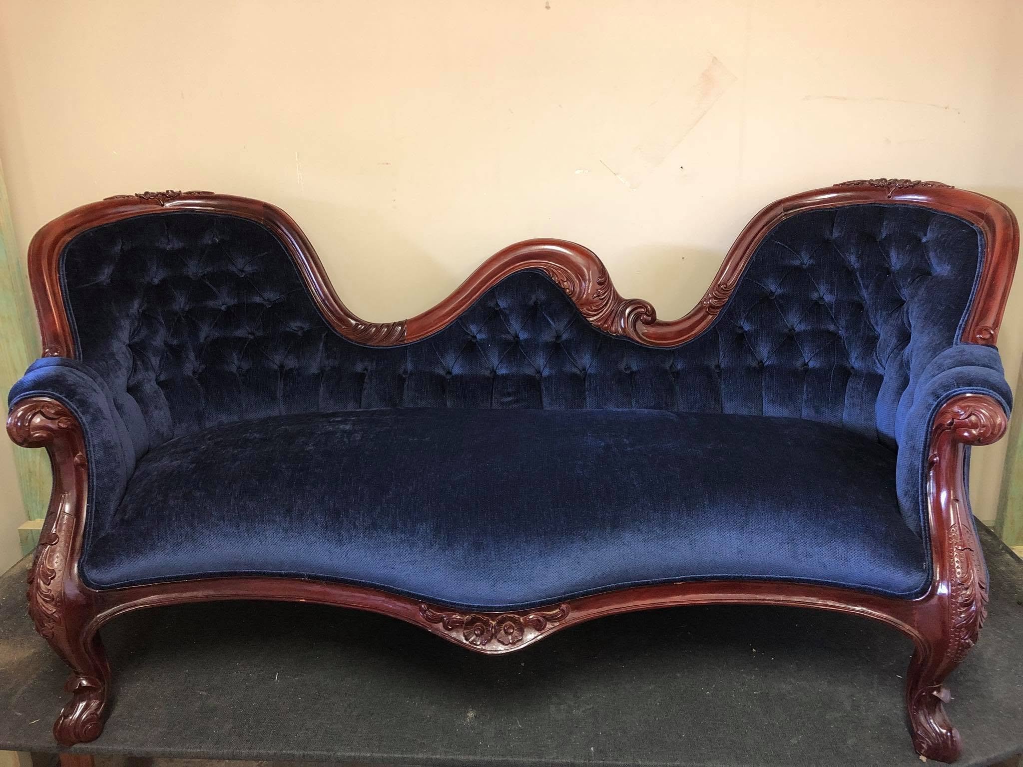An antique wooden couch with dark blue velvet upholstery and ornate carved wood details on the frame.
