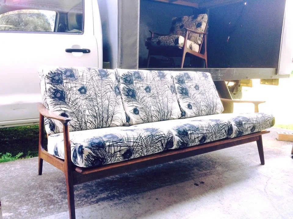Mid-century modern sofa with a peacock feather pattern fabric in an outdoor setting, with a vintage chair on a truck bed in the background.