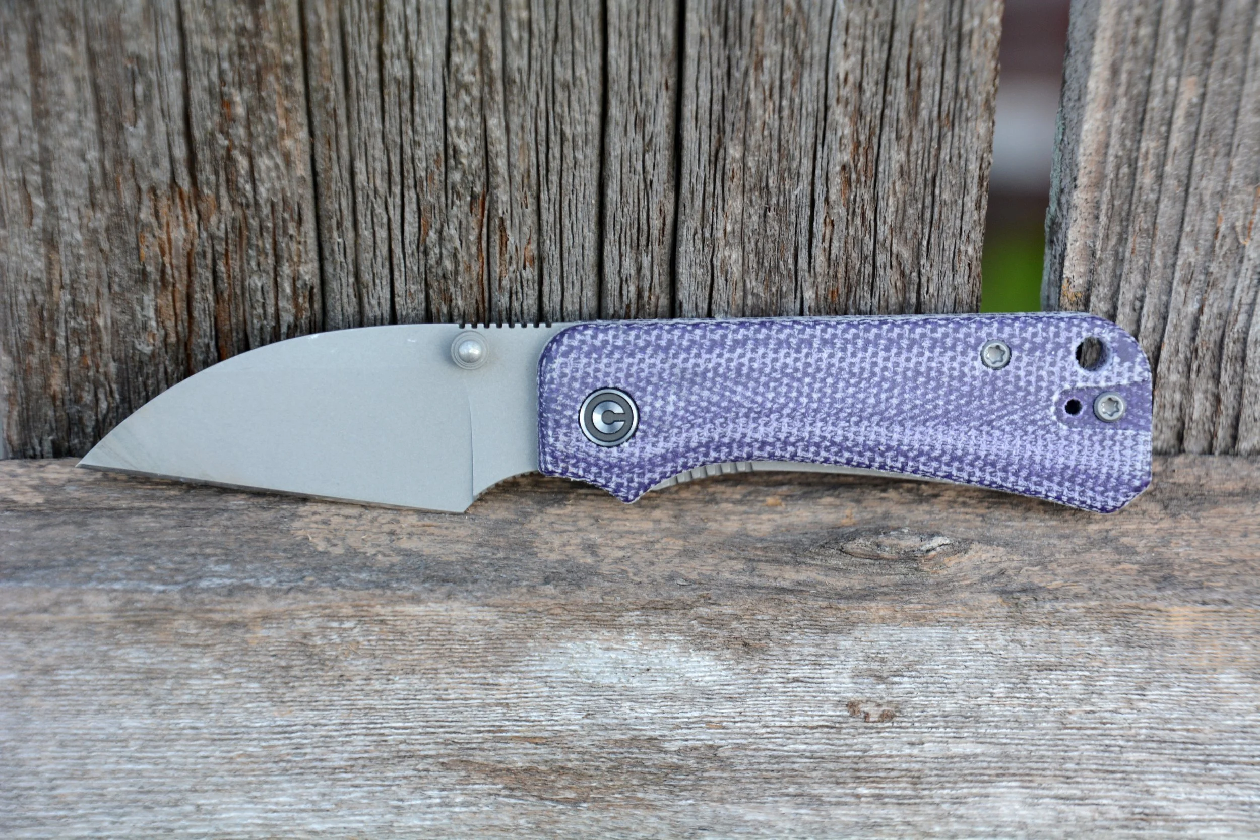 Close-up of a folding pocket knife with a partially opened blade, placed on a weathered wooden surface.