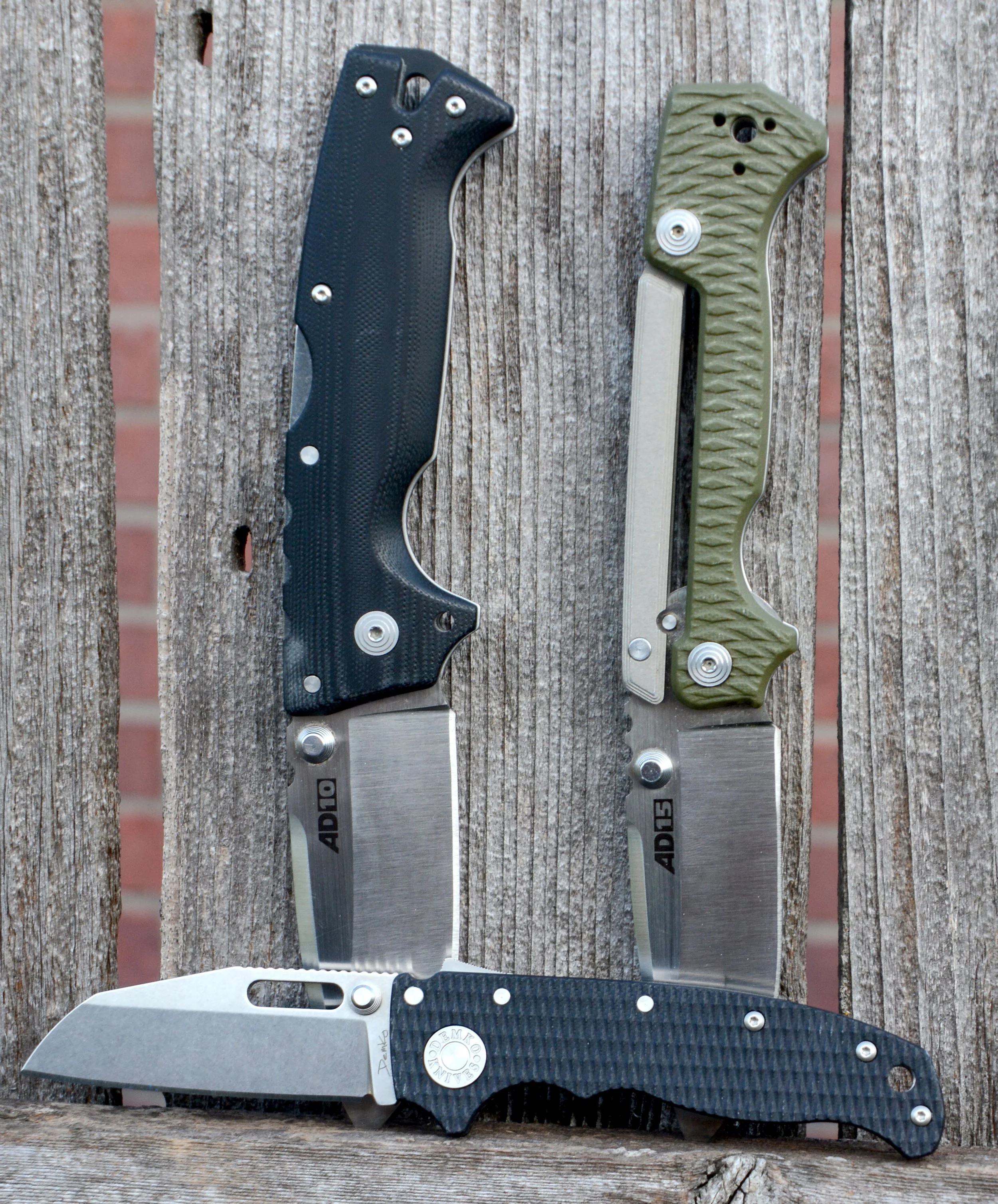 Two folding pocket knives with black and green handles, open and placed on a wooden surface.
