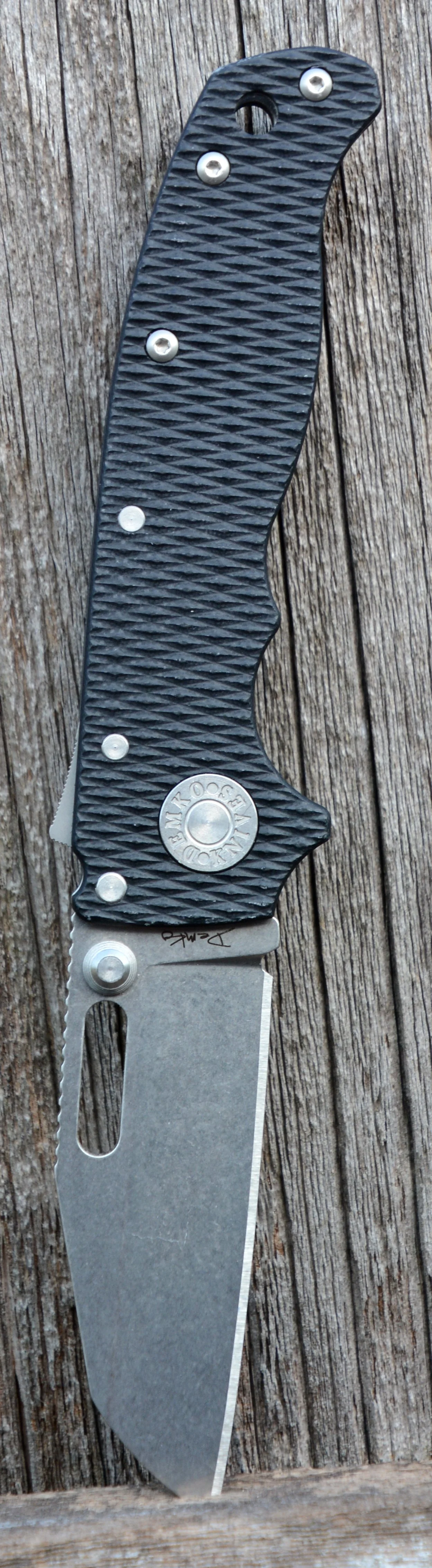 Close-up of a folding pocket knife with a black textured handle and a partially extended blade, resting on a weathered wooden surface.