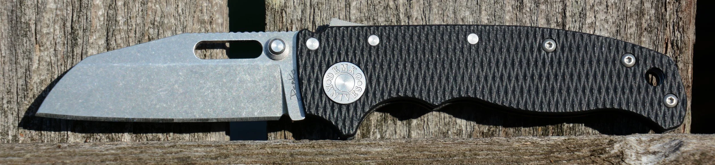 A folding pocket knife with a silver blade and black textured handle resting on a wooden surface.