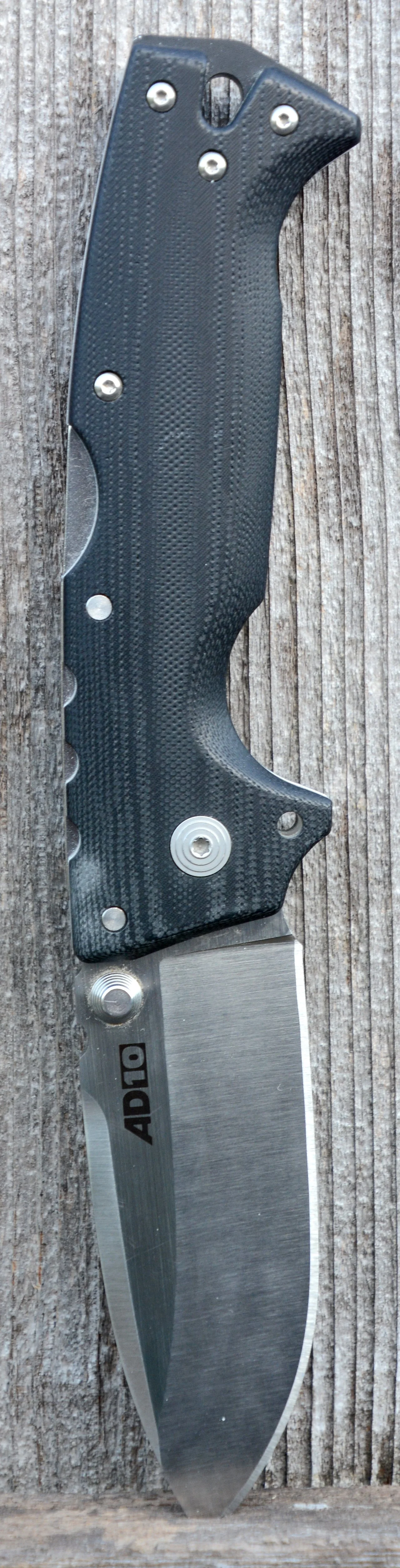 A fixed-blade folding knife with a black textured handle and silver accents, lying on a weathered wooden surface.