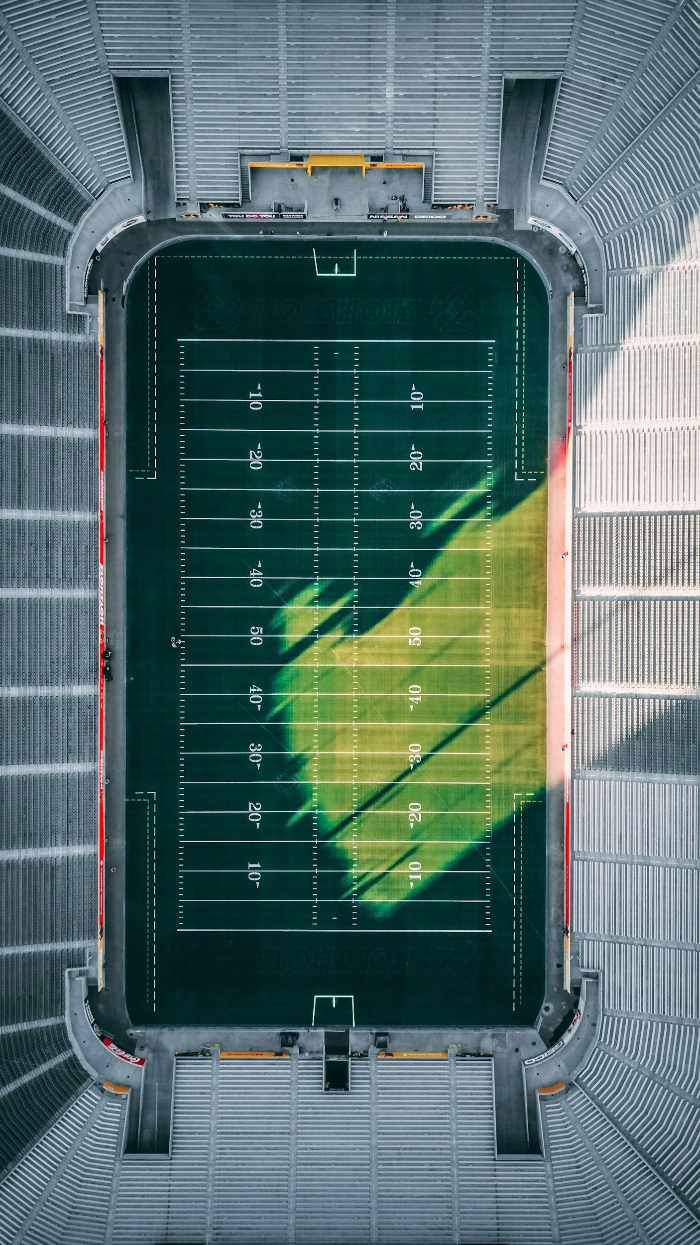 An aerial view of a football stadium field, showing the field with yard lines and seating surrounding it.