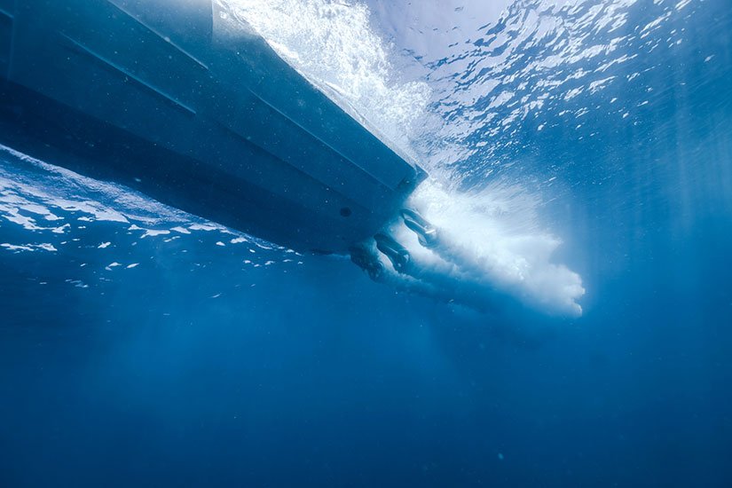 Underwater view of a boat's hull slicing through the water, creating a splash and wake.