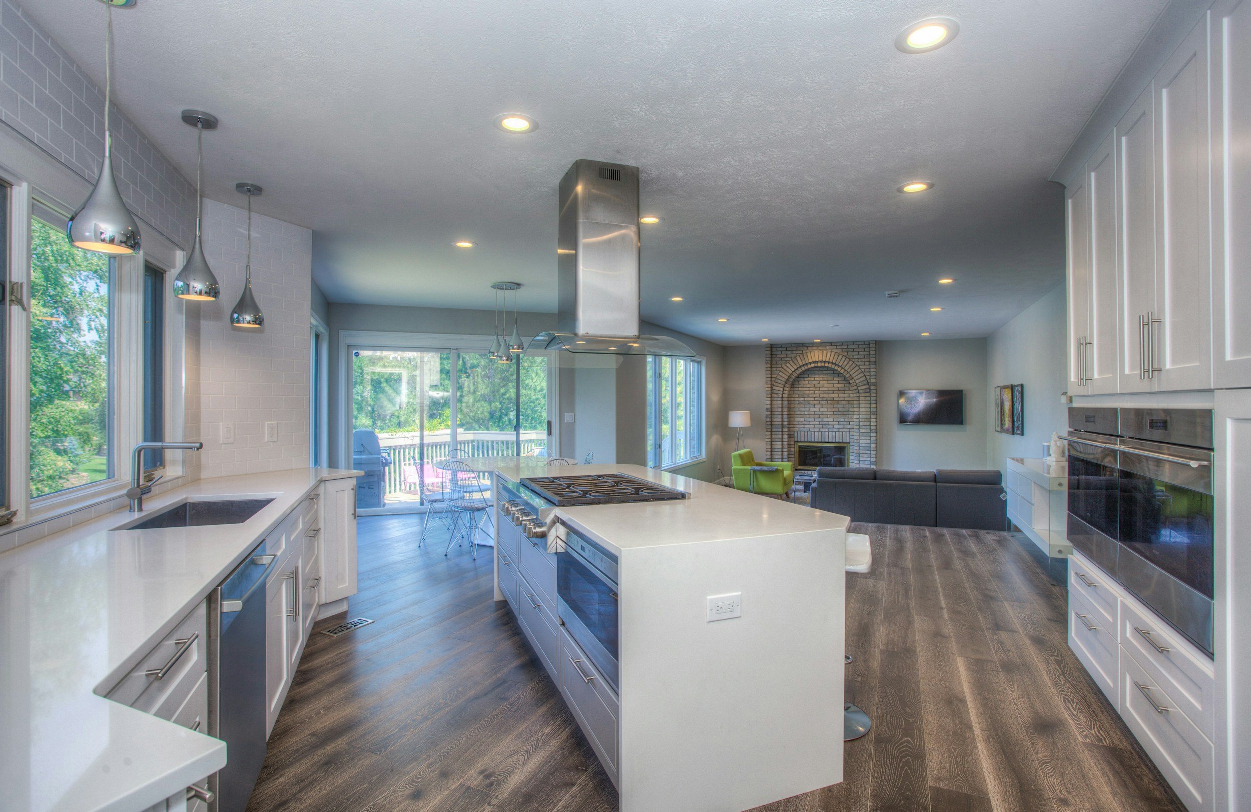 Open-concept kitchen and living room with large windows, white cabinets, island, dining table, fireplace, and modern decor.
