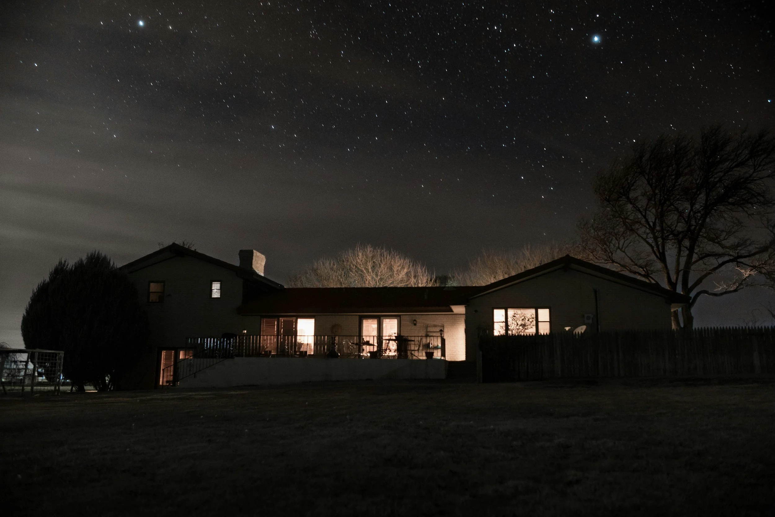 Nighttime scene of a residential backyard with a house, trees, and visible stars in the sky.