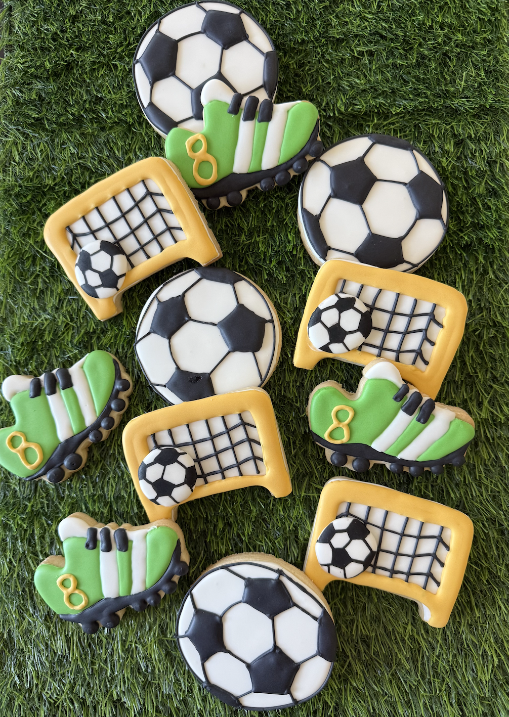 Decorated cookies with soccer and sports themes on green grass background, including soccer balls, goal nets, and cleats with the number 8.