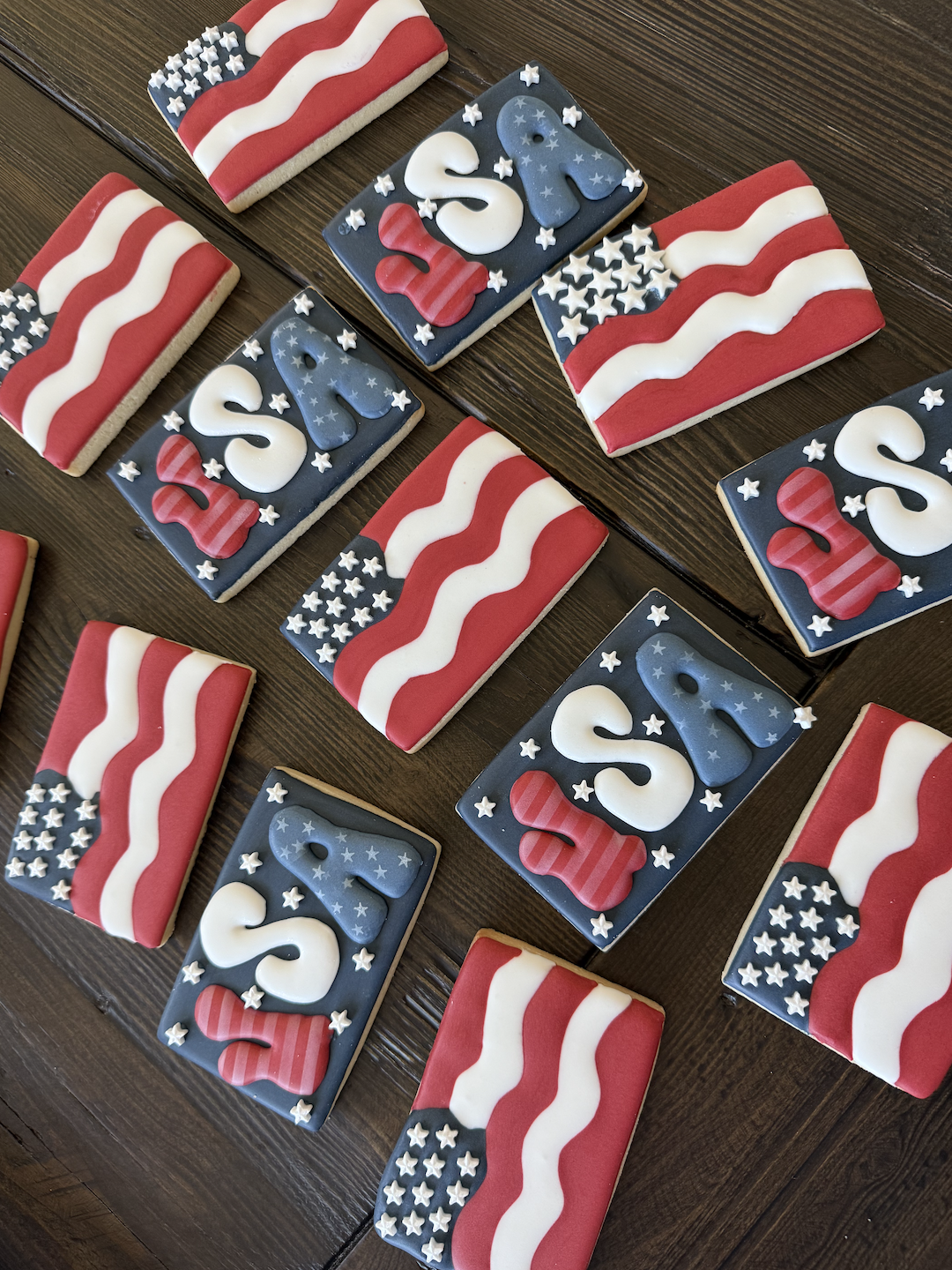 Decorated cookies with American flag theme, featuring red, white, and blue colors, stars, stripes, and the words 'U.S.' on some cookies, arranged on a wooden surface.