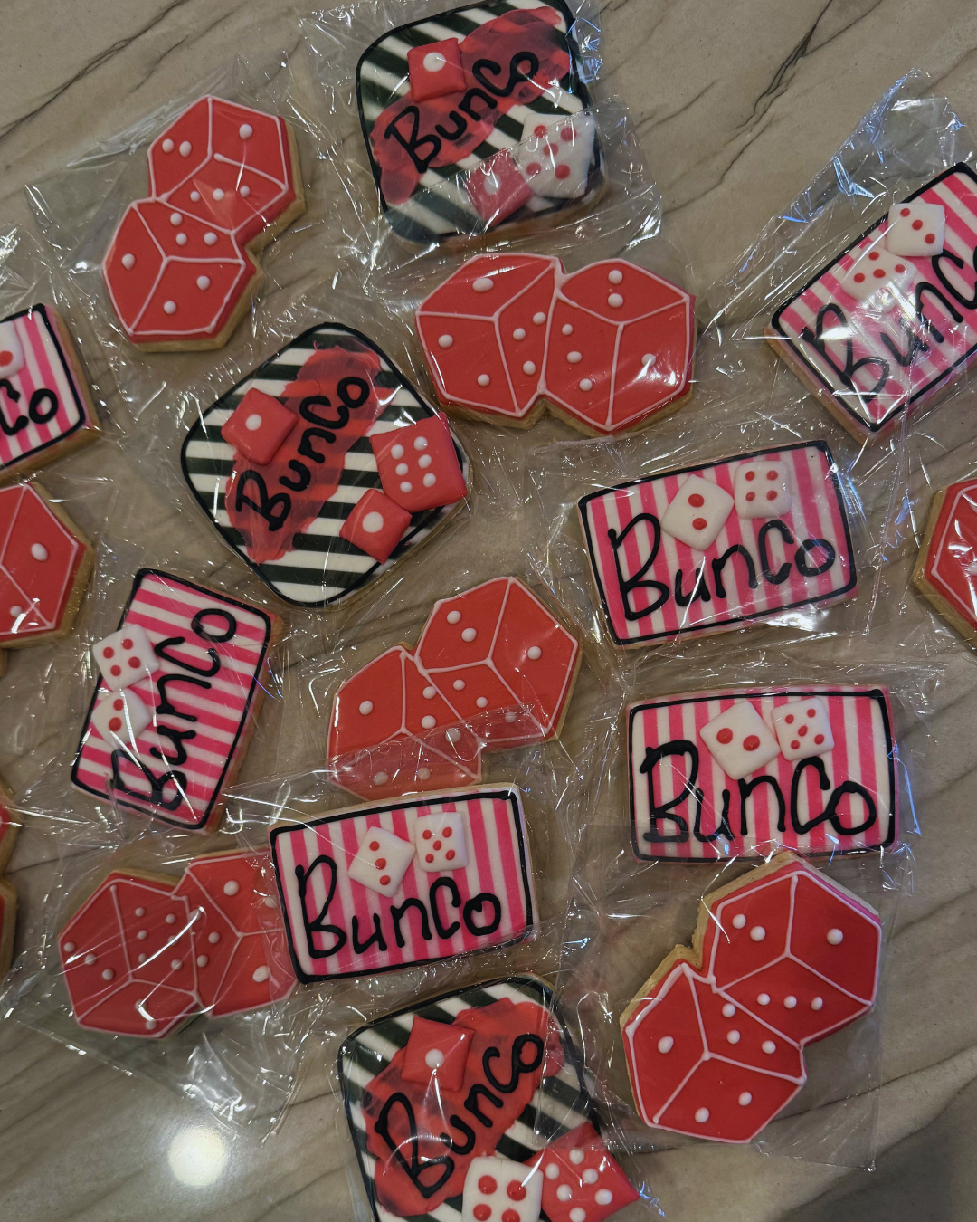 Decorated cookies with dice and bingo themes, wrapped in clear plastic, on a table.