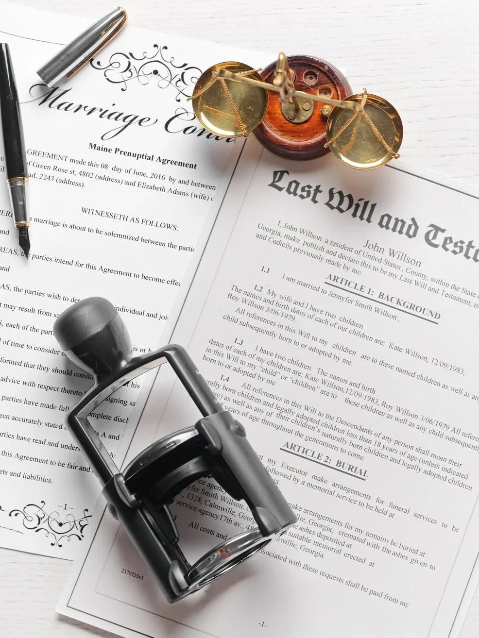 A marriage contract, a last will and testament, a fountain pen, a set of tiny gold sunglasses, and a black stamp on a white background.