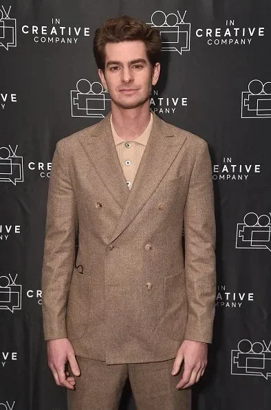 Young man in beige suit standing in front of a black backdrop with logos for 'In Creative Company'.