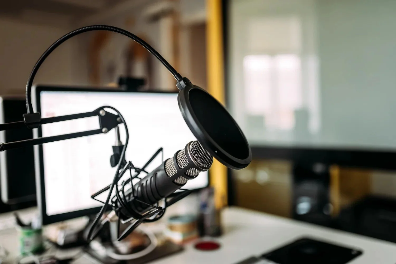 A professional microphone with a pop filter on a desk in front of a computer monitor, setup for recording or streaming.