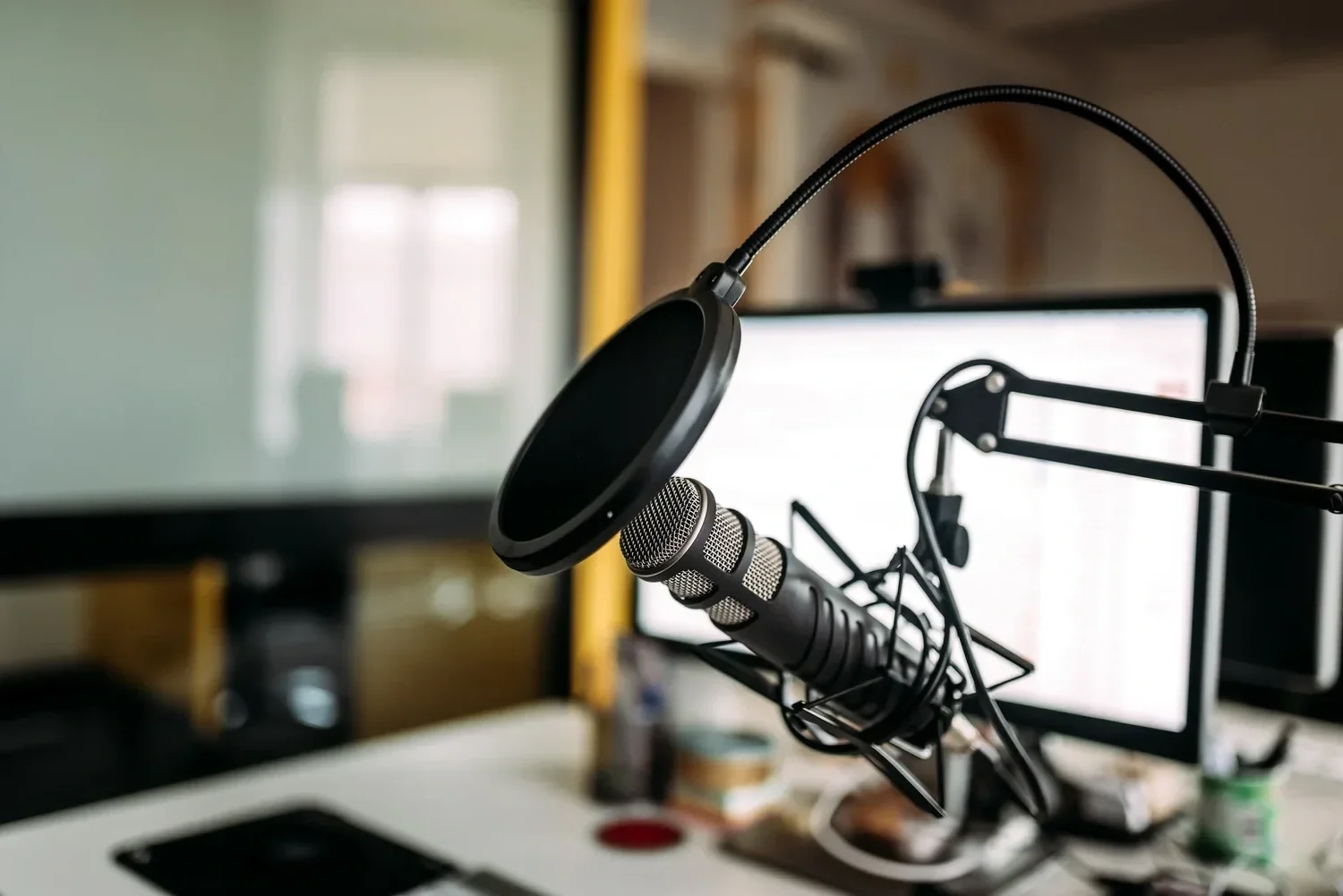A microphone with a pop filter mounted on a stand in front of a computer monitor on a desk