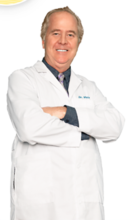 A male doctor with gray hair wearing a white lab coat, standing with arms crossed, smiling