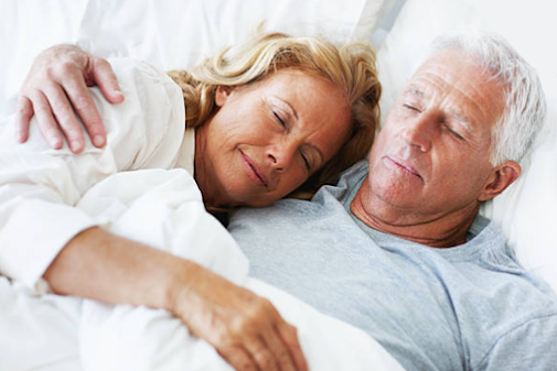 A senior couple lying in bed together, smiling and embracing each other.