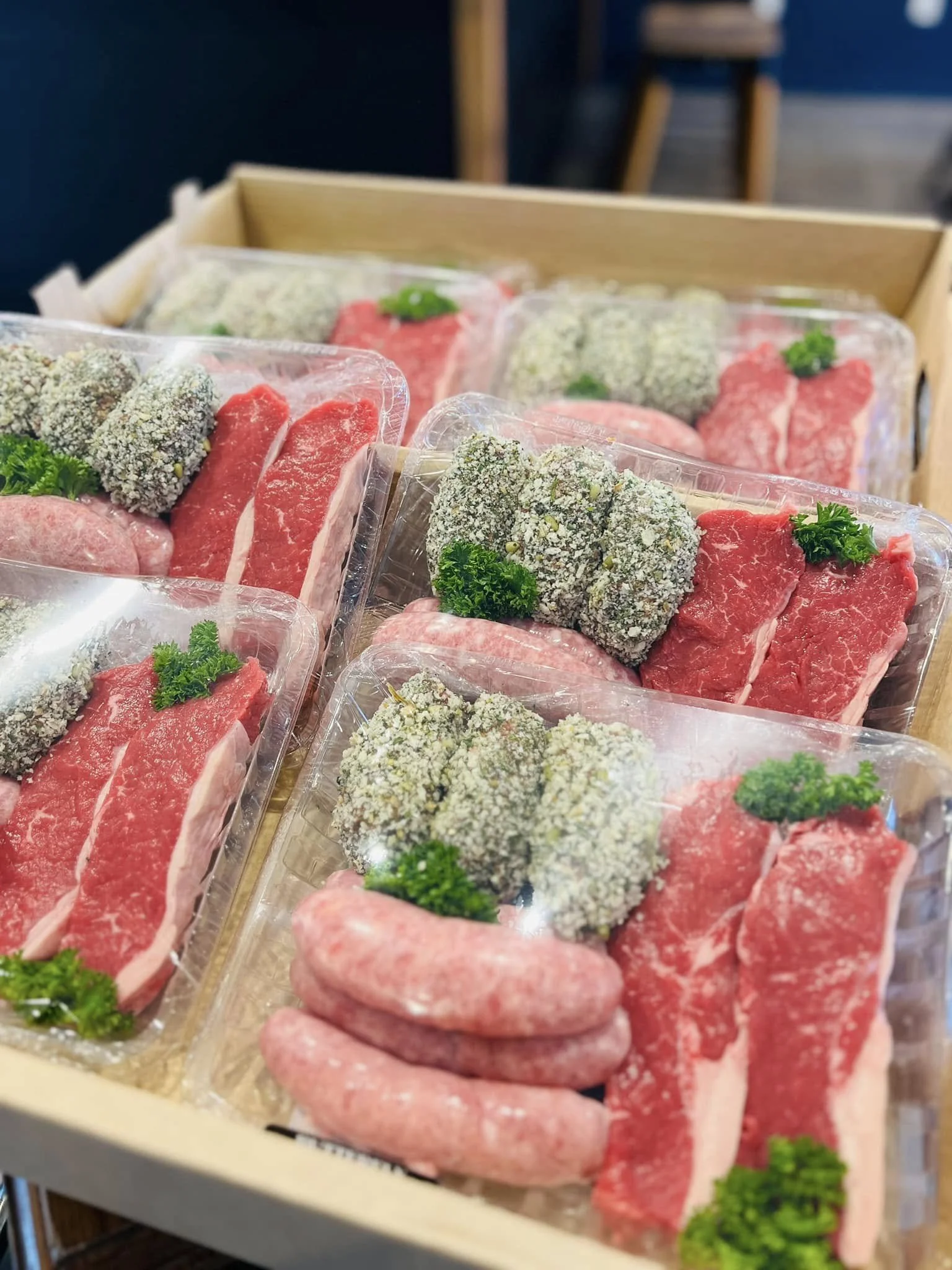 Brochured display of various raw meat cuts, including beef and pork, garnished with parsley, in clear plastic trays on a wooden table.