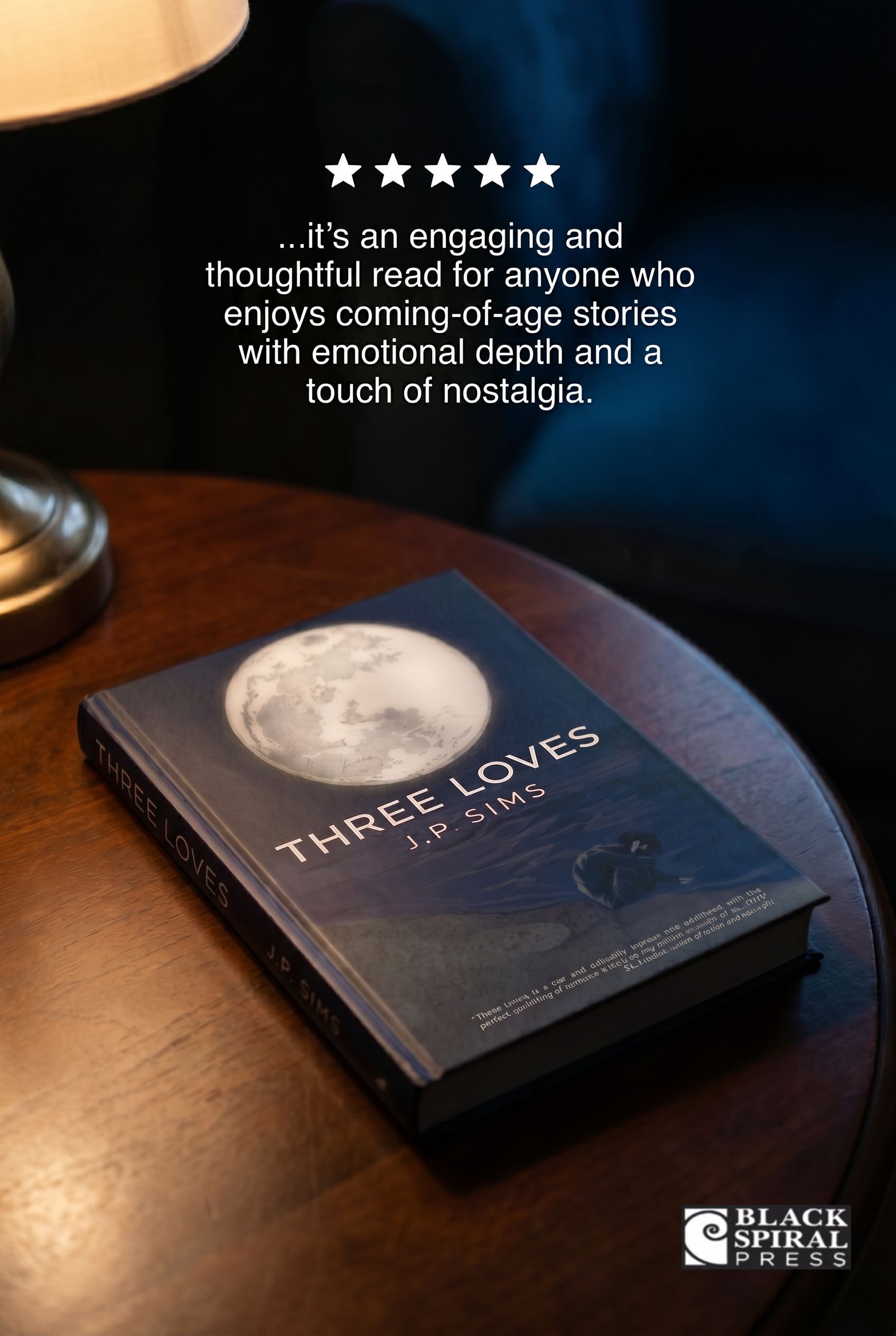 A book titled 'Three Loves' by J.P. Sims is resting on a wooden surface. A lamp and part of a moon-themed coaster are also visible in the background.