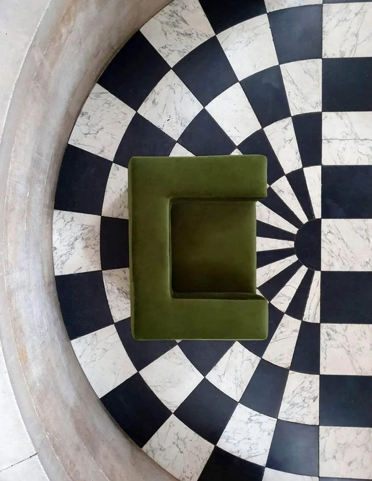 Overhead view of a green armchair on a black and white radial patterned floor with a beige circular border.