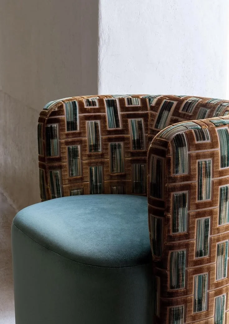 Close-up of a modern armchair with a patterned fabric backrest and a teal upholstered seat.