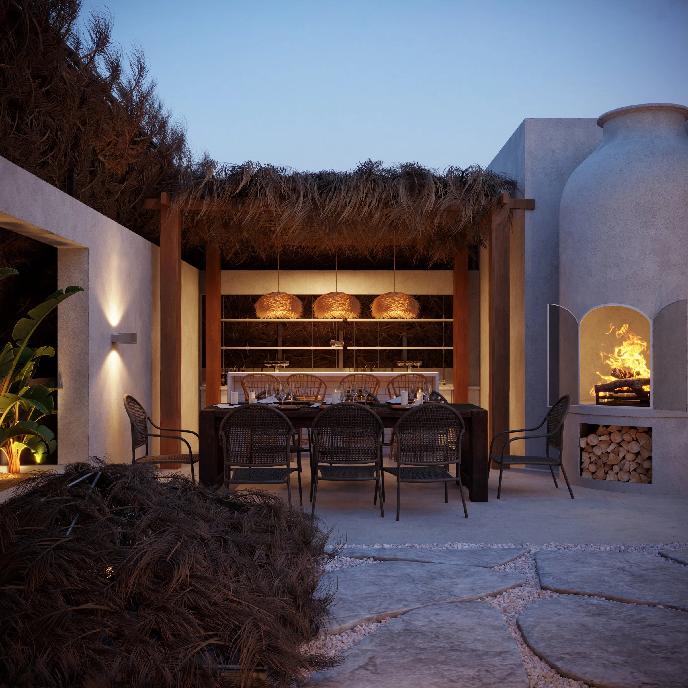 A patio area with a dining table and chairs, hanging pendant lights, a fire feature with flames, and architectural elements including white stucco walls and a thatched roof structure, during evening or dusk.