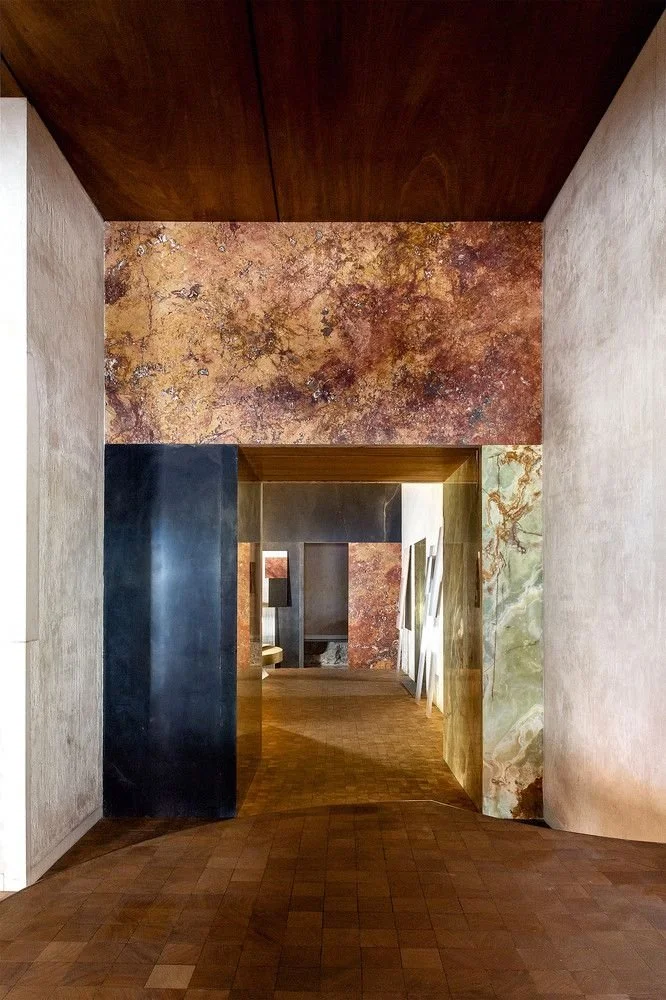 Interior view of an art gallery or museum with doorways, textured walls with marble and painted finishes, and a wooden floor.