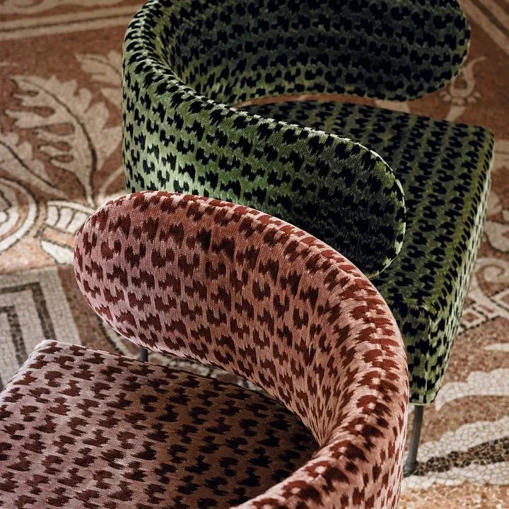Three upholstered chairs with patterned fabric in green, pink, and black colors, placed on a patterned carpet.