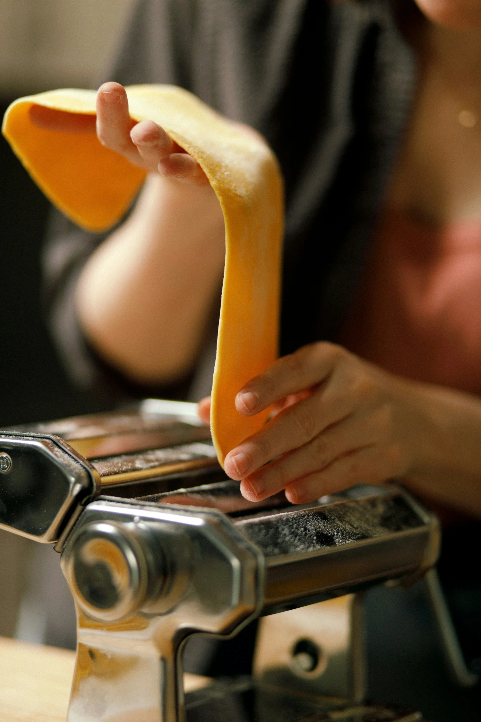 A person using a pasta machine to make sheets of pasta dough.