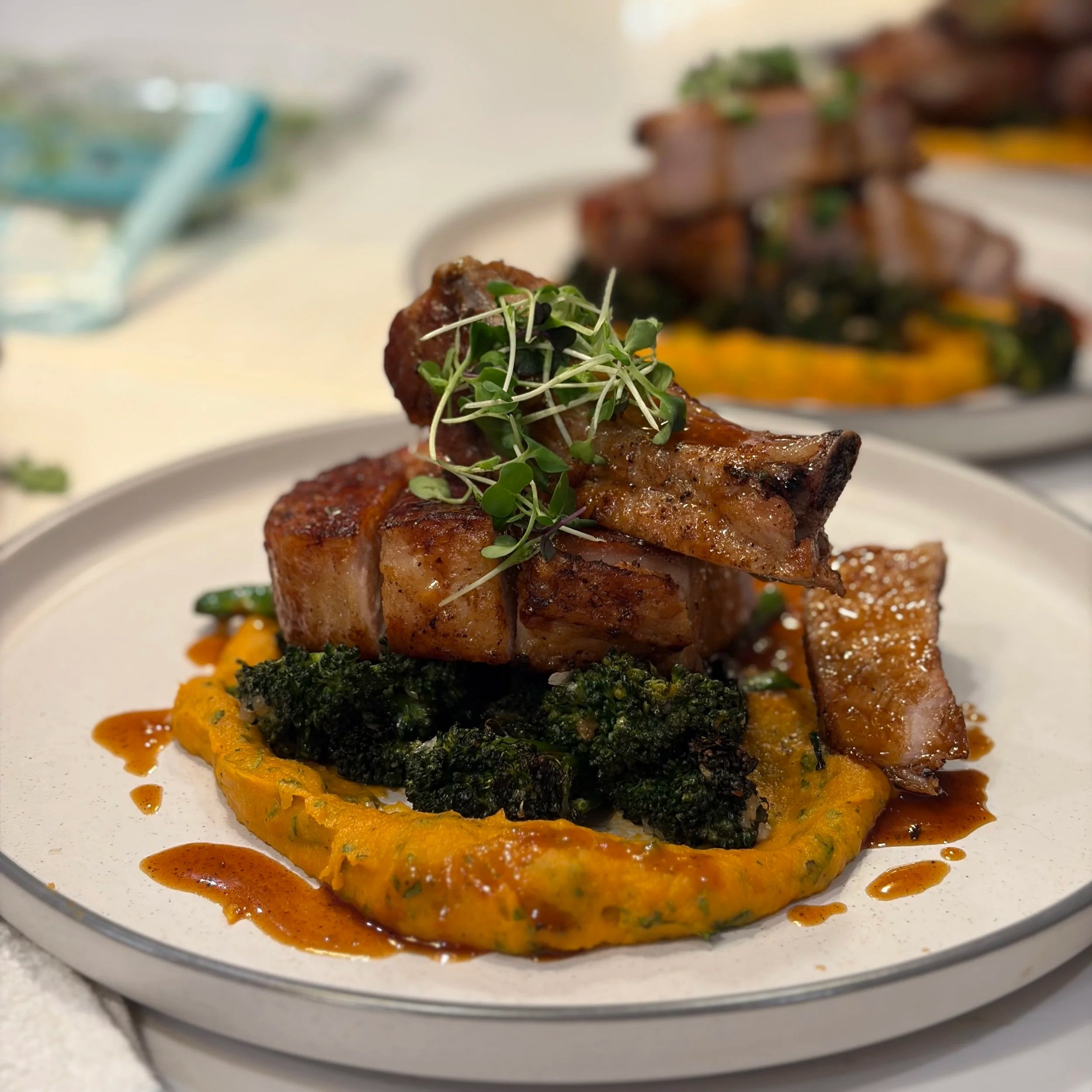Close-up of a plate with grilled meat garnished with microgreens, set on a bed of roasted vegetables and surrounded by sauce.