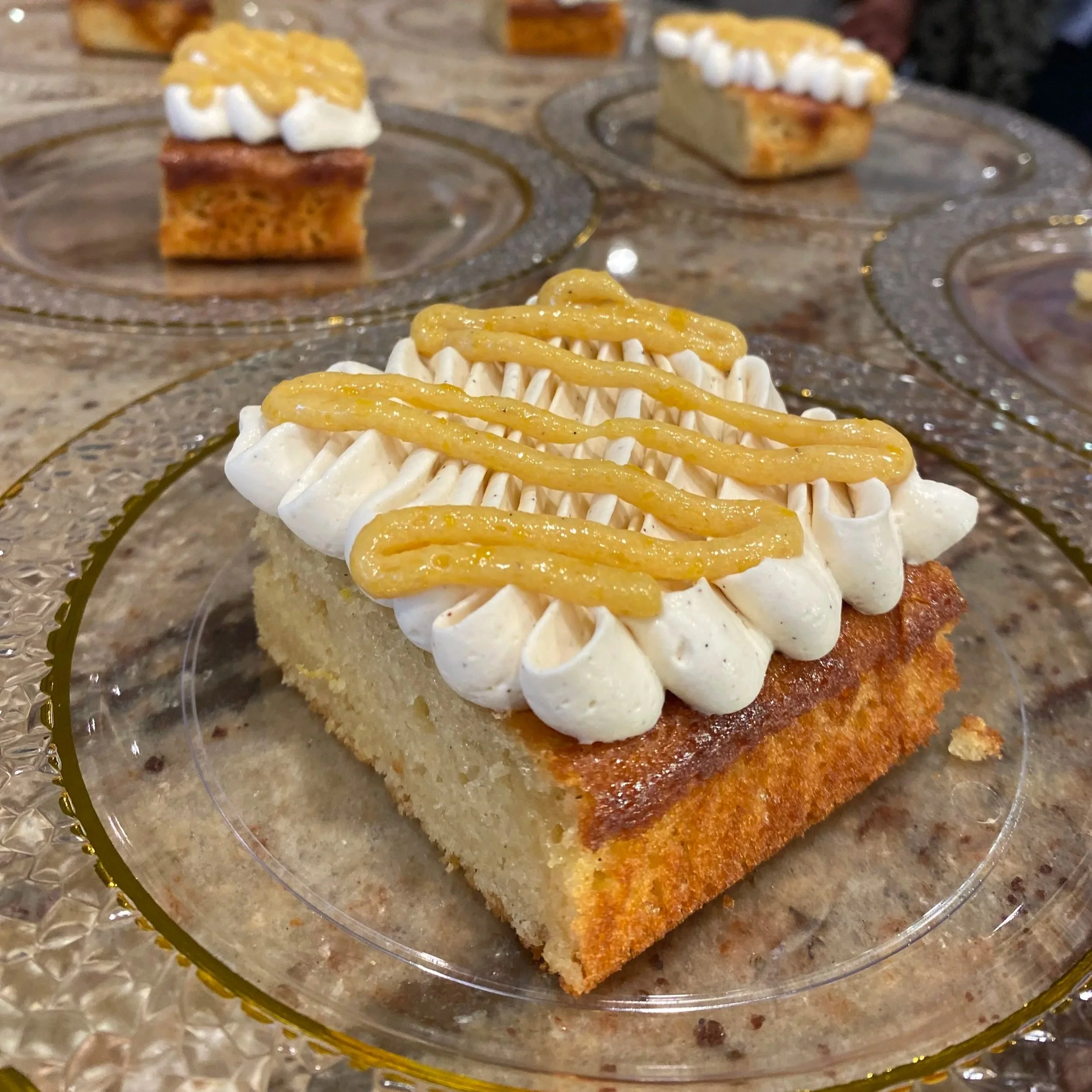 A close-up view of a small dessert topped with piped white frosting and a yellow glaze, placed on a clear glass plate.