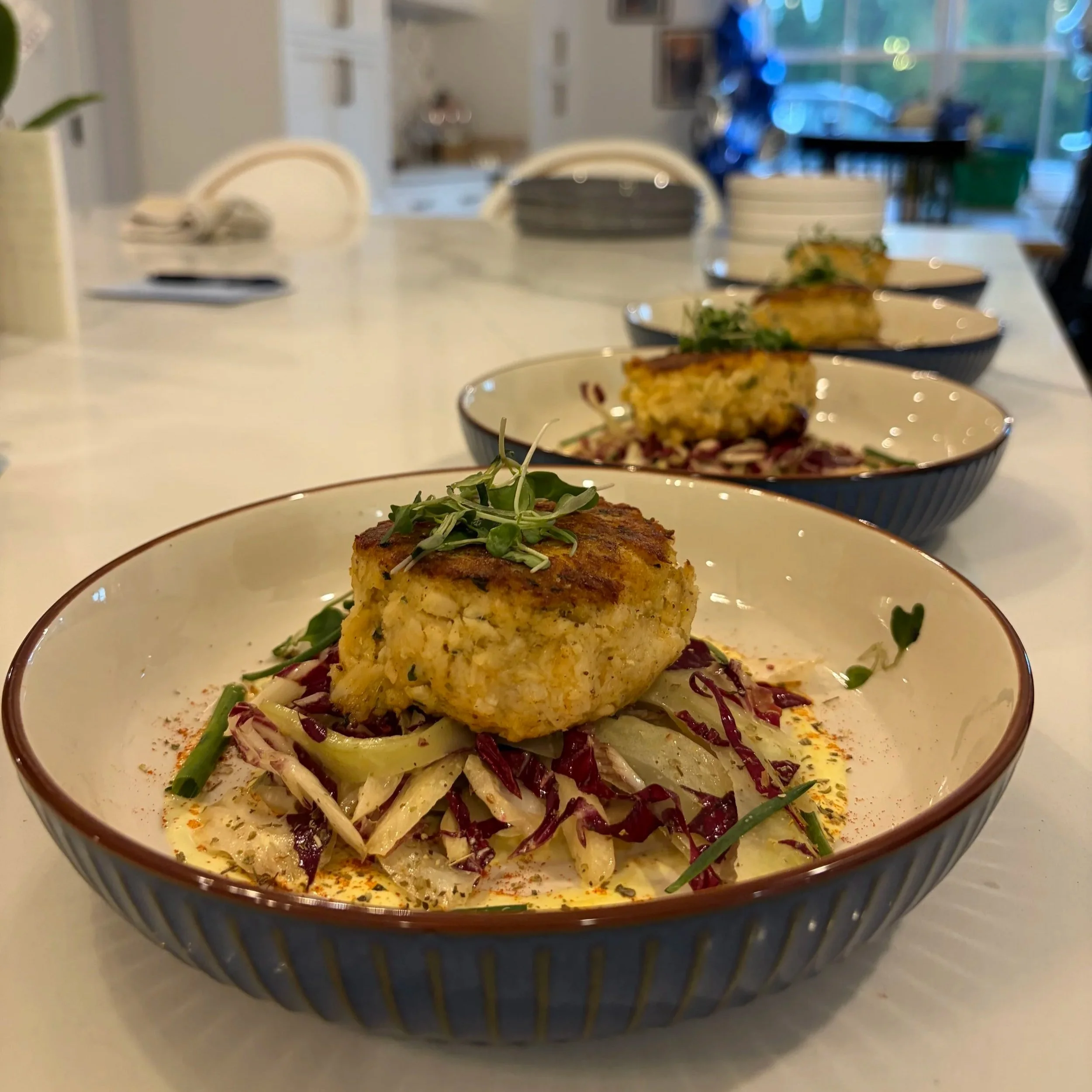 Close-up of a plate with a piece of baked fish garnished with microgreens, with several other similar plates in the background on a dining table.