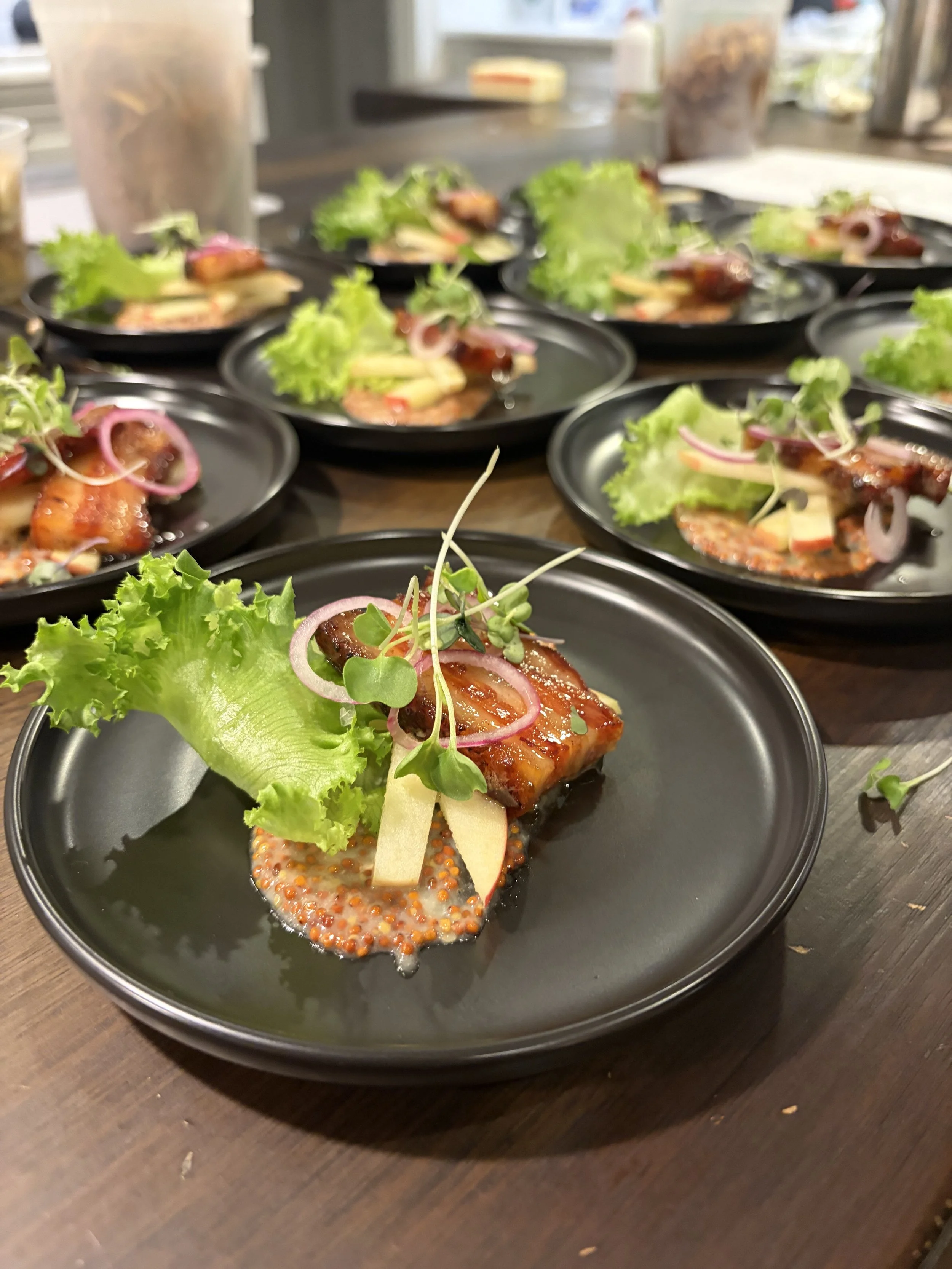 Plates of cooked salmon garnished with lettuce, red onion, and microgreens on black plates placed on a wooden table.