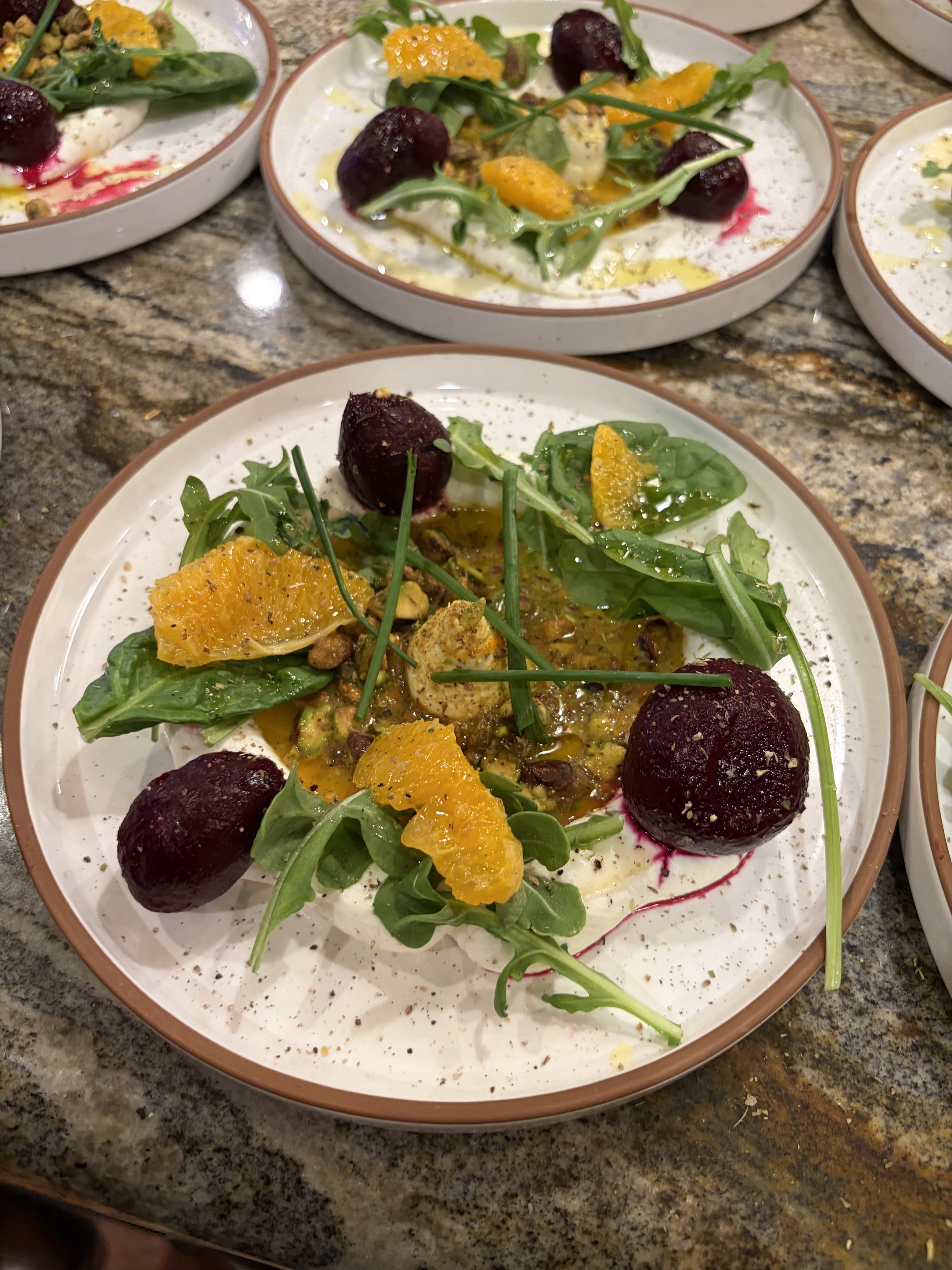 Plate of food with arugula, beet vegetables, orange slices, and dressing on a speckled granite countertop.