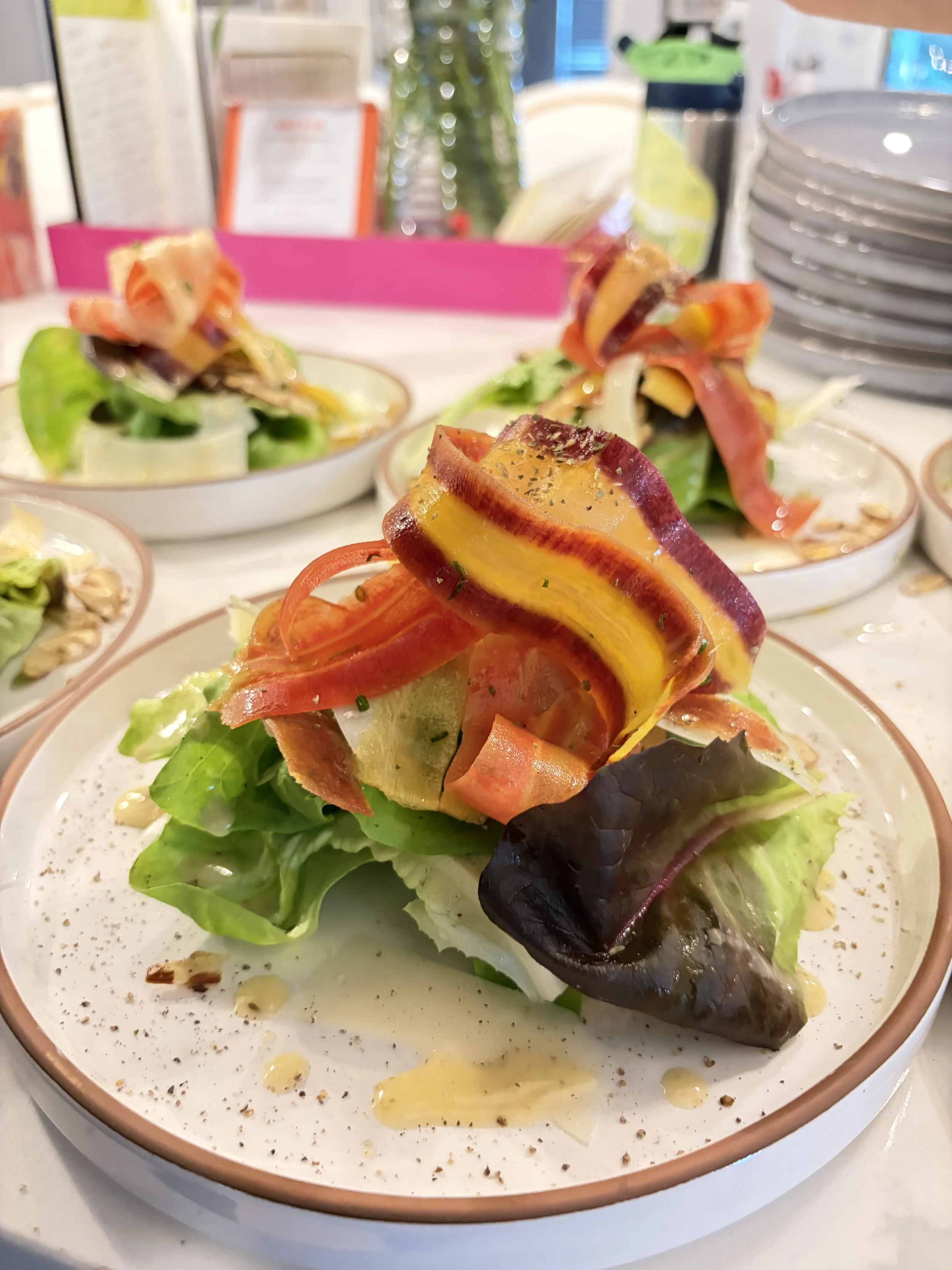 A plate of salad with mixed greens, roasted yellow and red peppers, and a dressing, presented on a white dish with speckled seasoning.