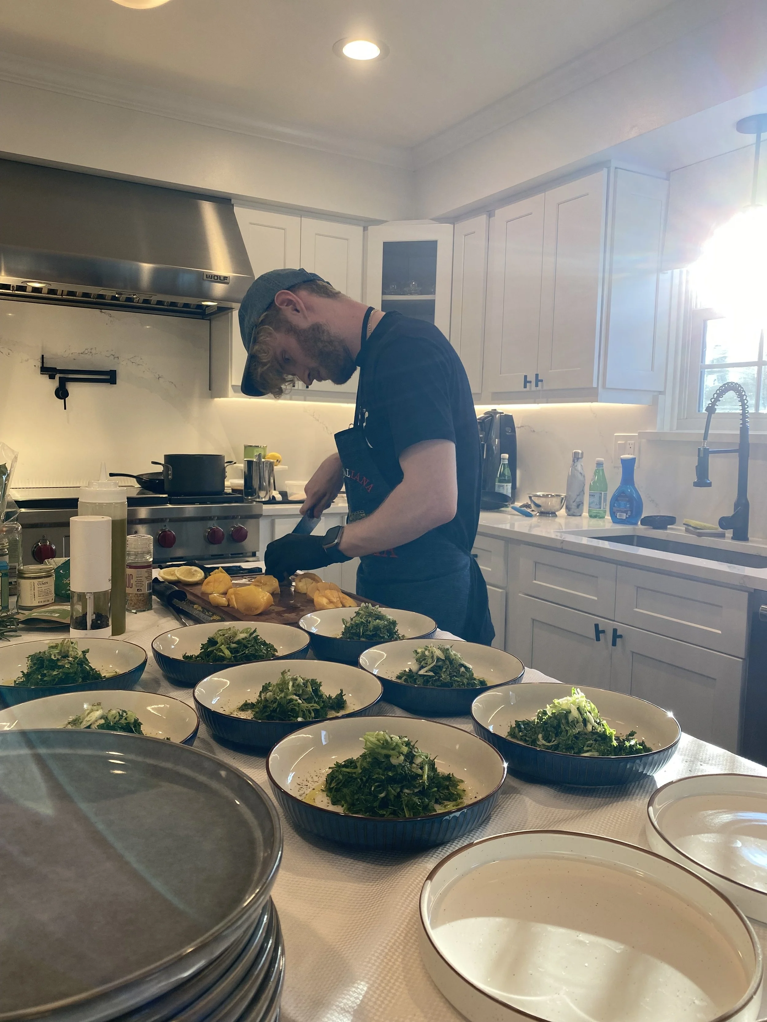 Man preparing salads in a kitchen with multiple bowls of salad on a table.