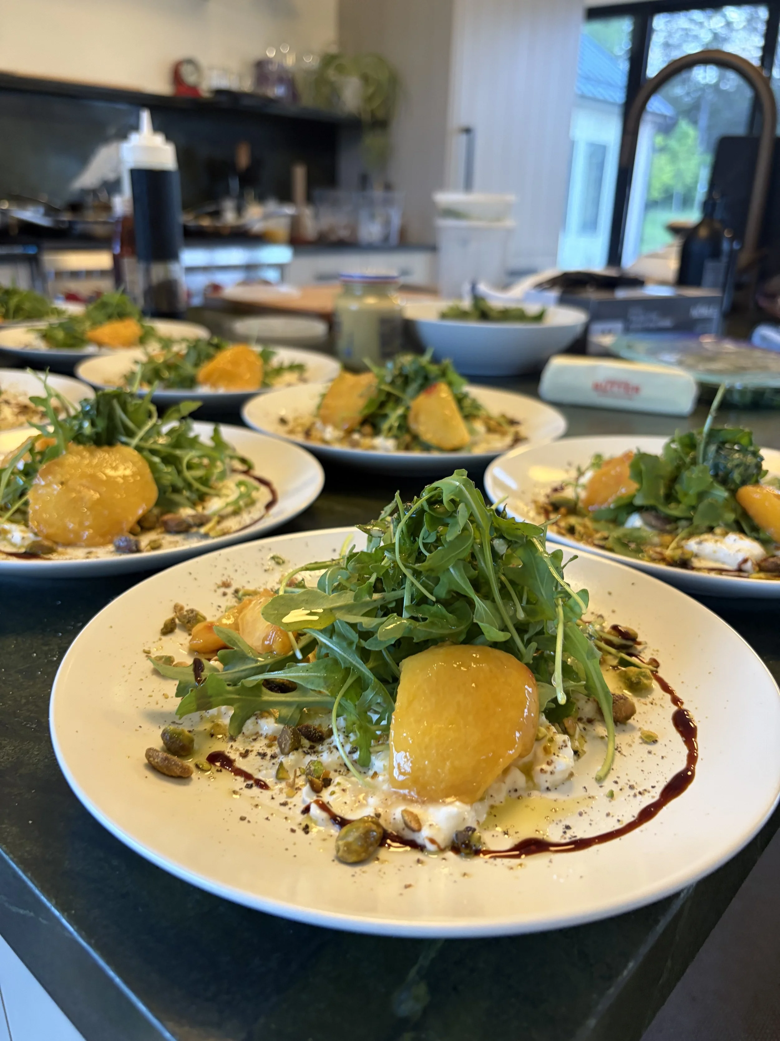 Plates of a salad with greens, yellow chunks of fruit or vegetable, and various toppings on a kitchen counter.