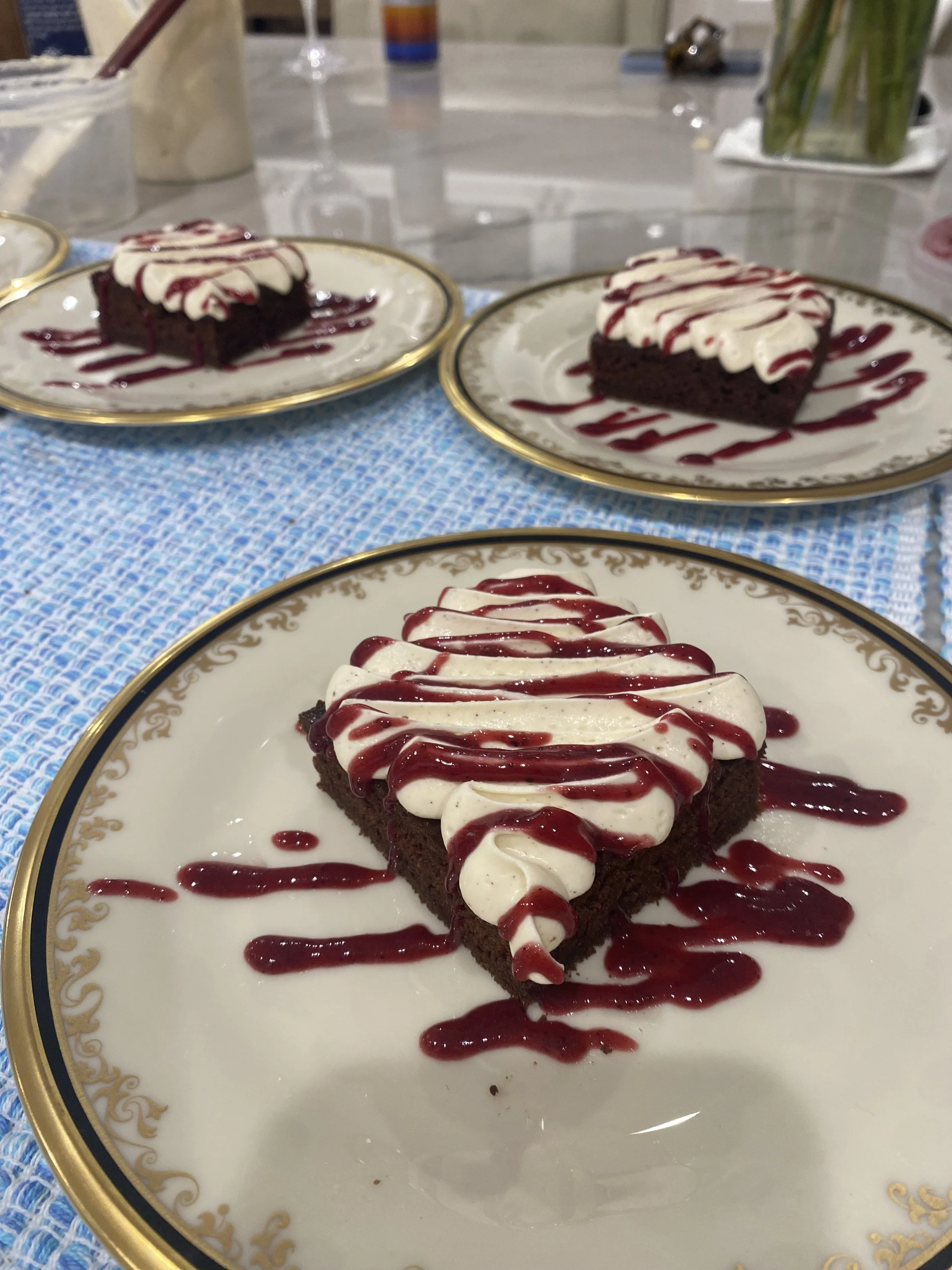 A slice of chocolate cake with white icing and raspberry sauce drizzled on top and around on an ornate white and gold plate.
