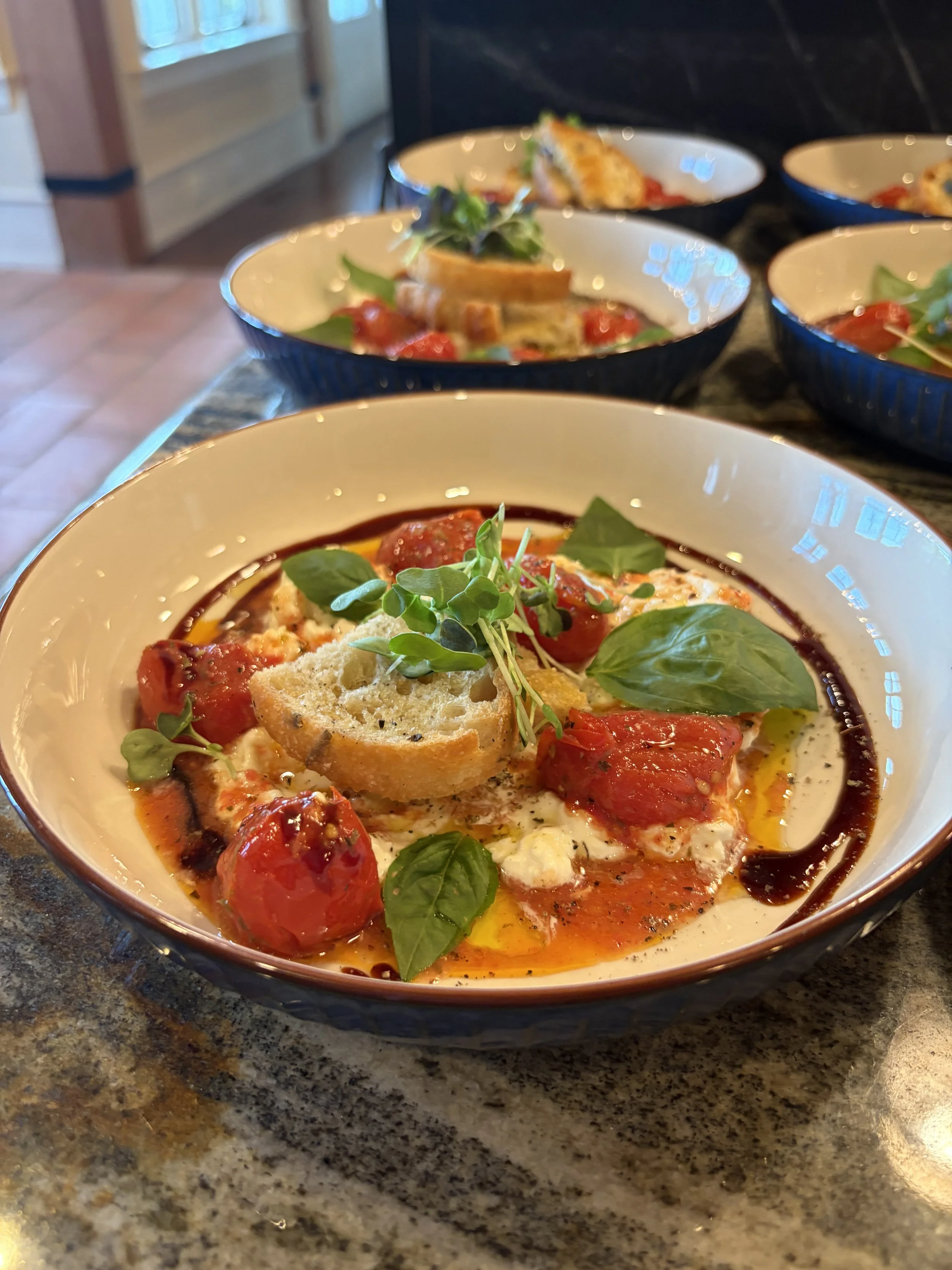 A bowl of tomato basil soup garnished with microgreens, a basil leaf, and a bread crouton, with a drizzle of balsamic glaze.