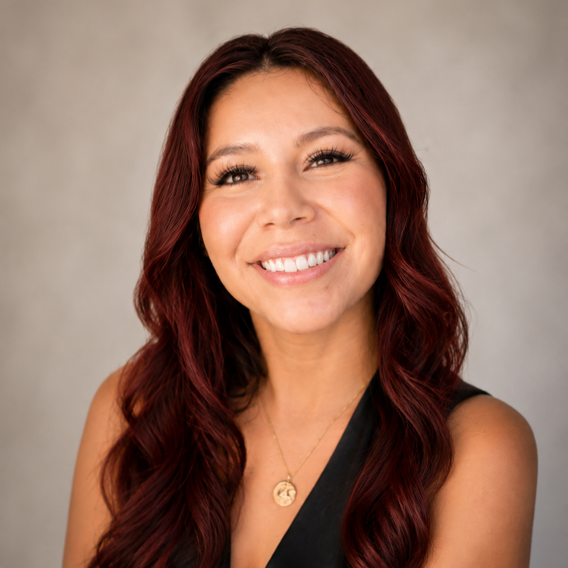 A woman with long, wavy, red hair smiling and showing her teeth.