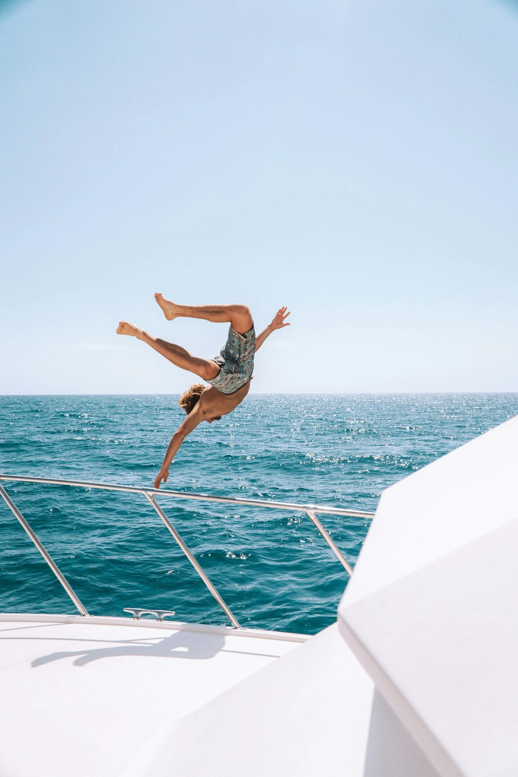 A person performing a handstand on the deck of a boat, with water and sky in the background.