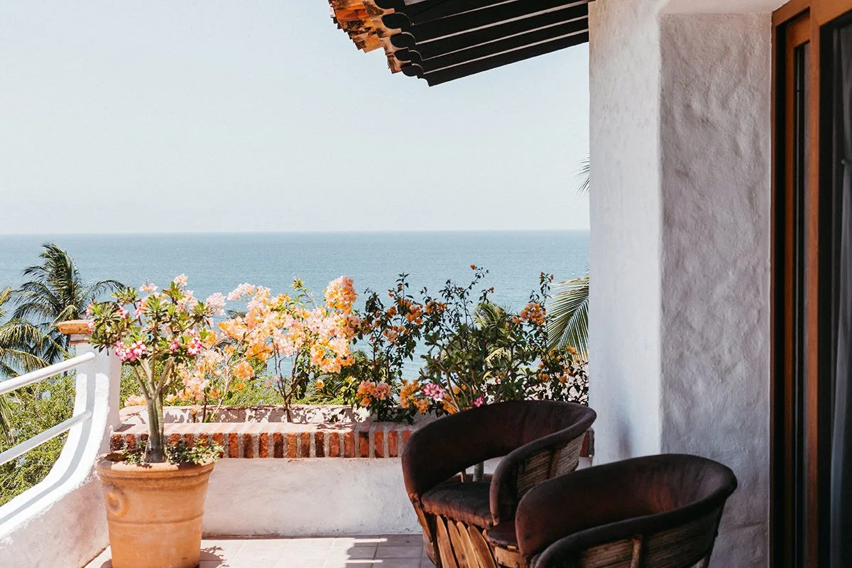 View from a balcony overlooking the ocean with potted flowers and patio furniture.