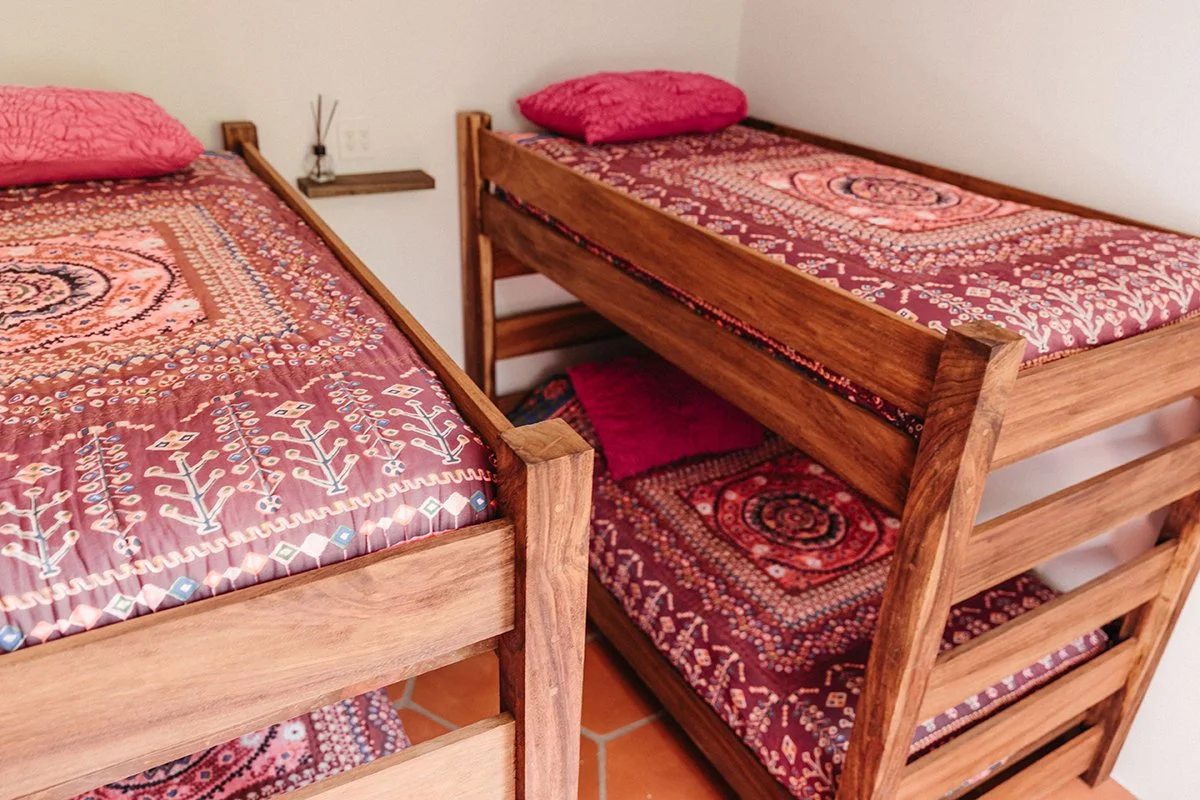Two wooden bunk beds with patterned pink and red bedding and matching pillows in a bedroom.