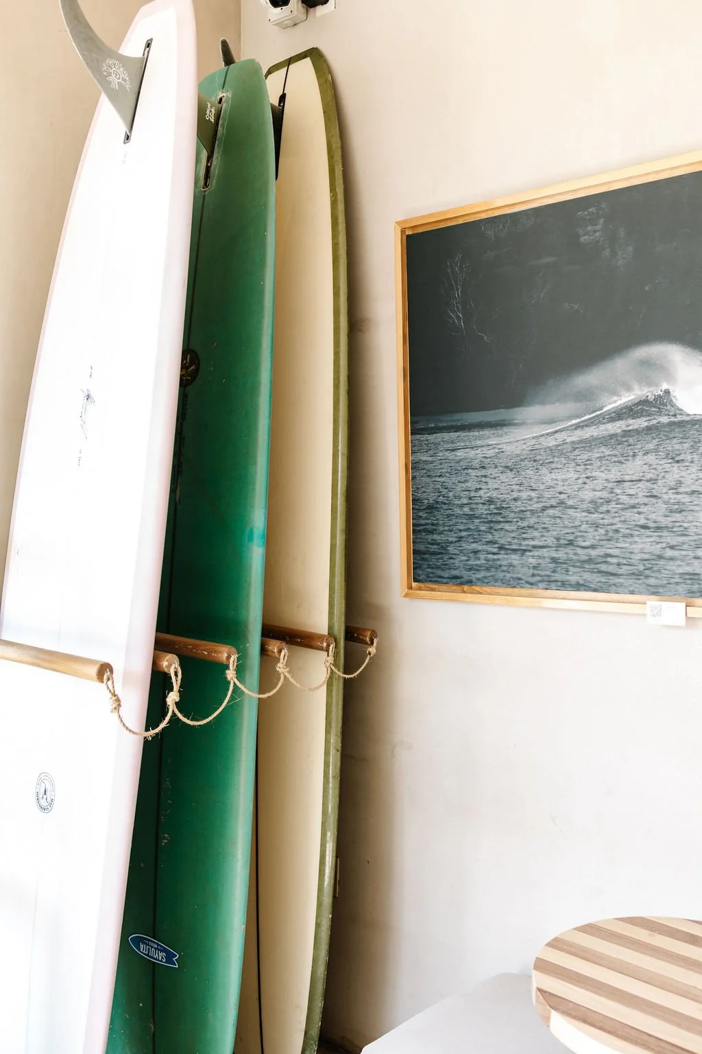 Four surfboards propped against a wall next to a framed black-and-white ocean photograph on a white wall.
