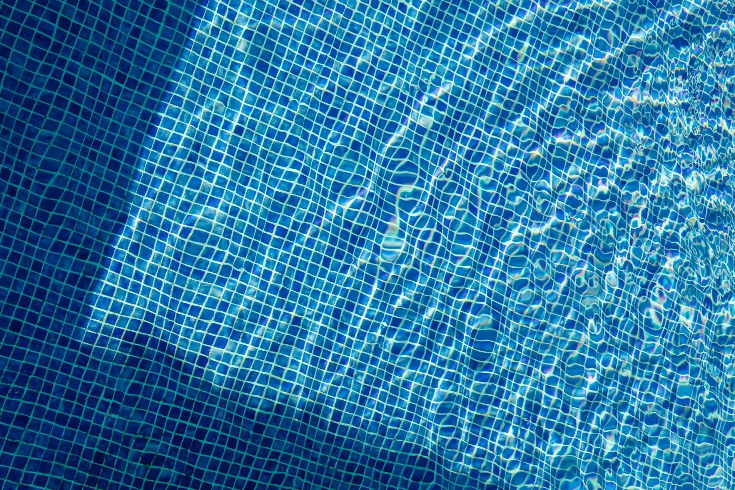 Close-up of a tiled swimming pool with sunlight reflecting off the water surface.