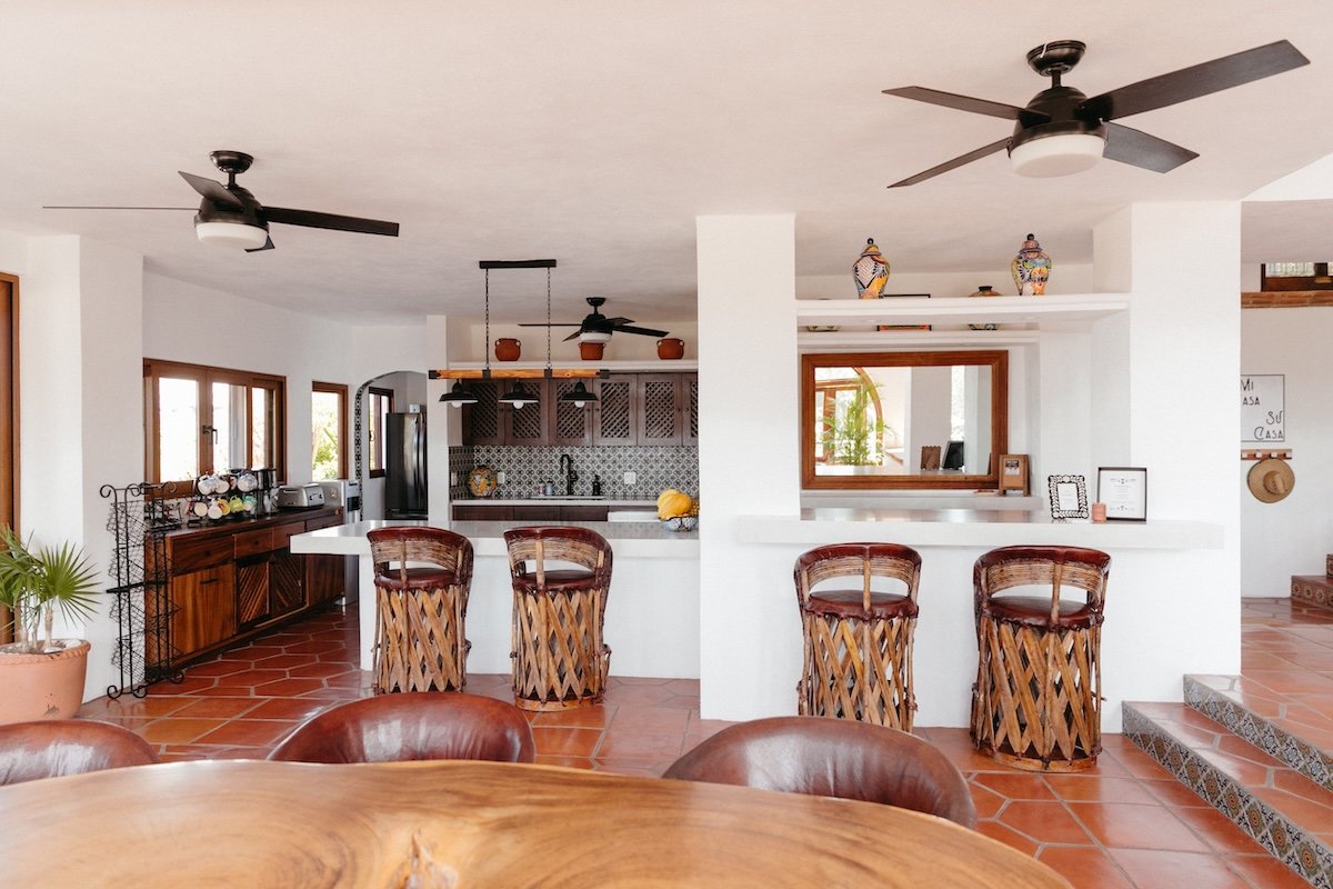 Kitchen and dining area with terracotta tile floors, wooden bar stools, and ceiling fans.