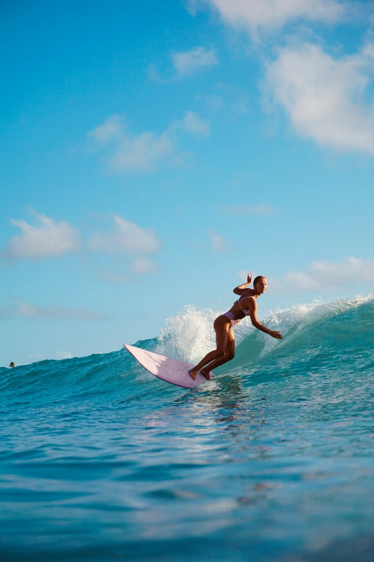 A woman surfing on a wave in the ocean under a partly cloudy sky.